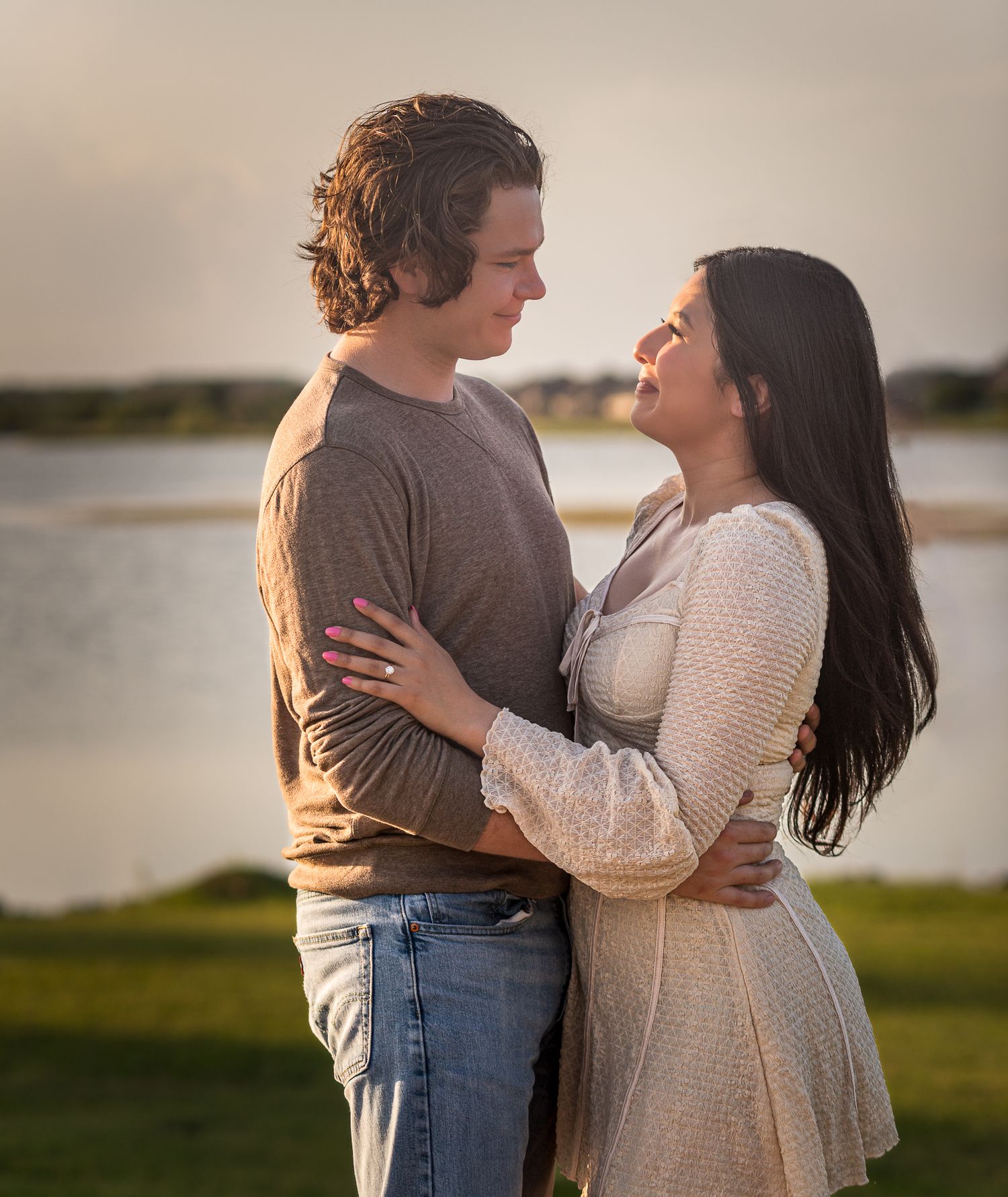 Couple embraces tenderly by a lake during golden hour.