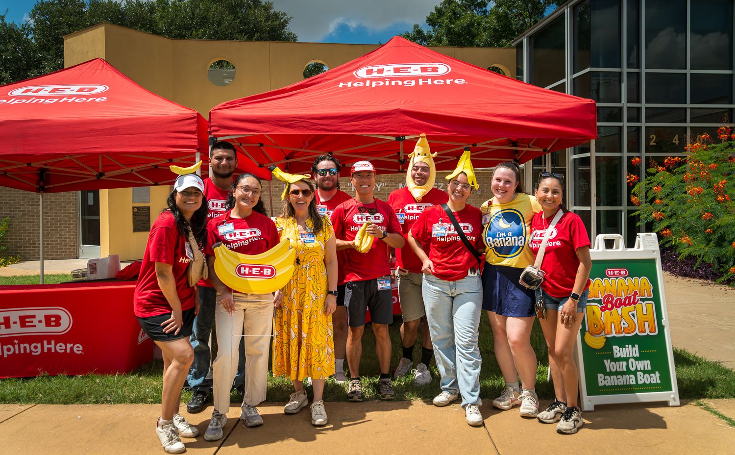 Group of volunteers gathered under red H-E-B branded tents at an outdoor community event.
