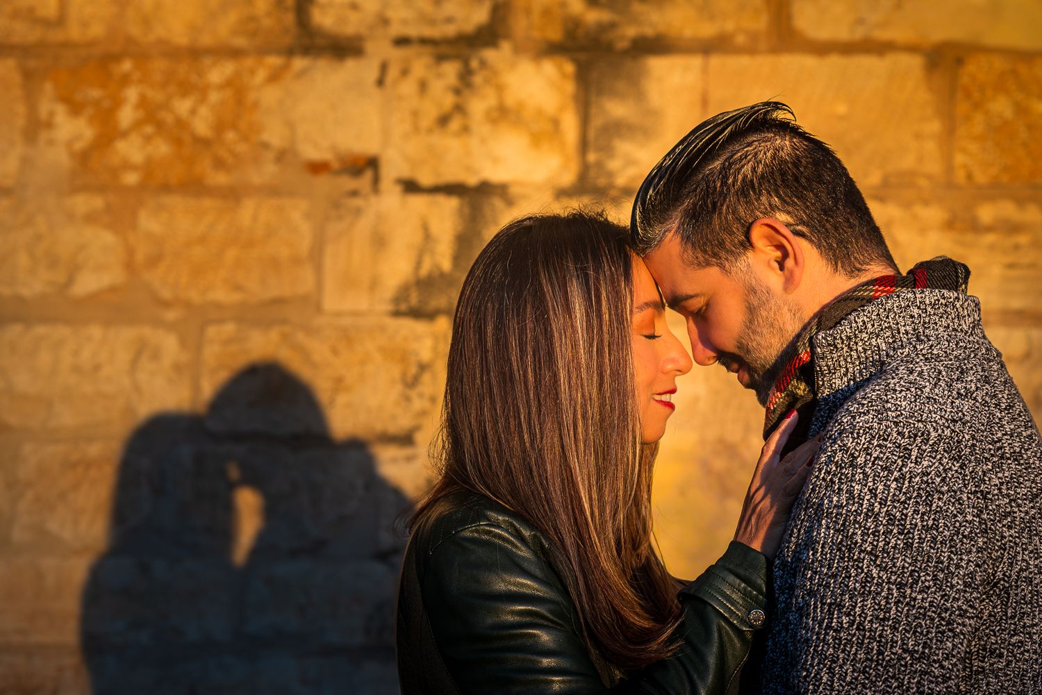 A romantic couple embraces against a rustic stone wall backdrop during golden hour.