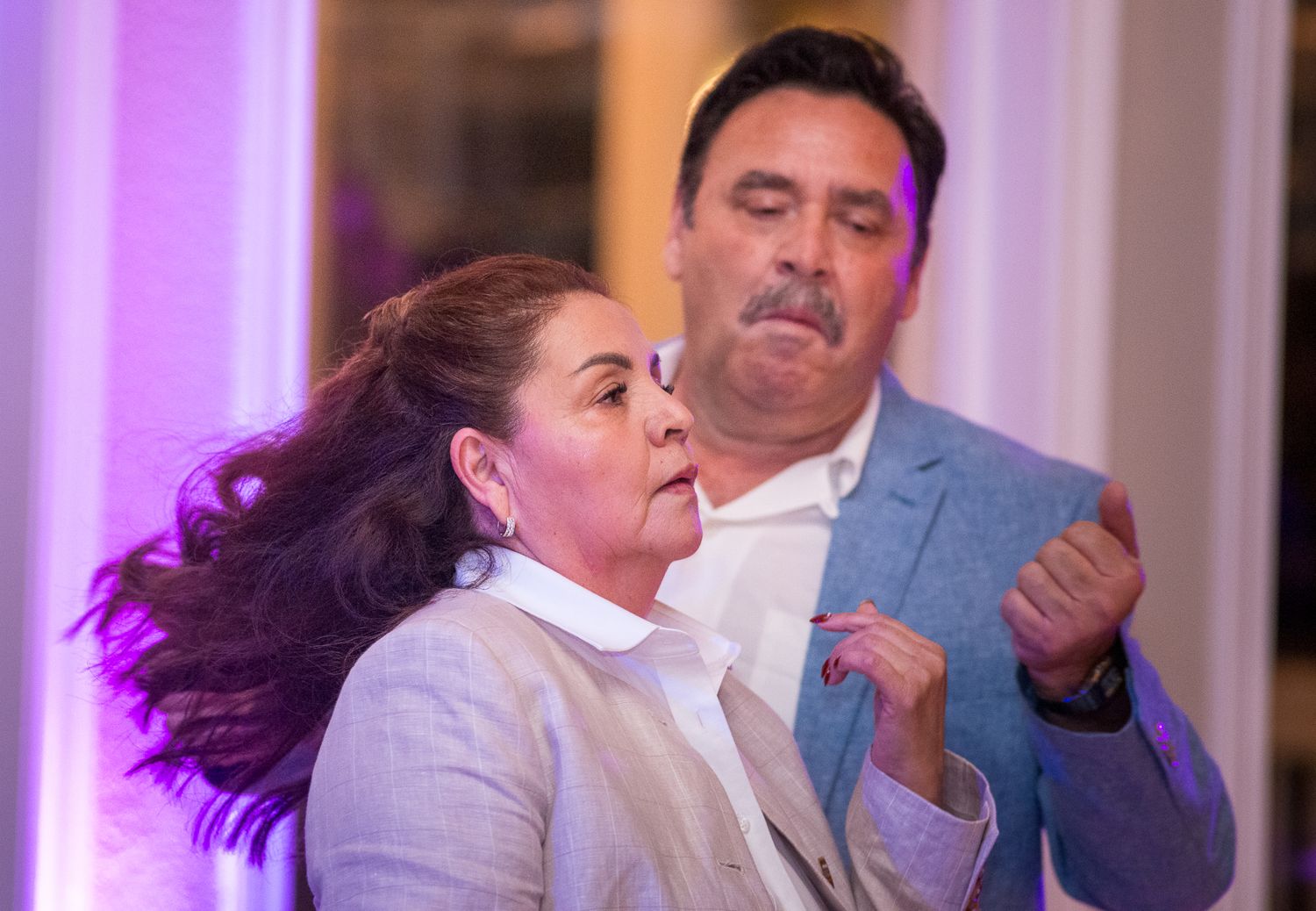 People dancing together at a lively wedding reception with purple lighting.
