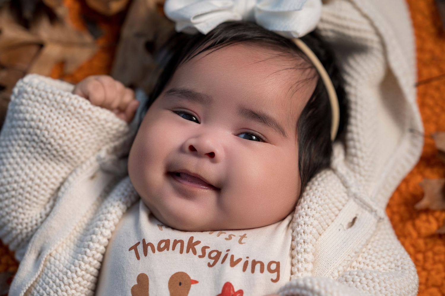 Baby wearing white knit clothing lying on textured orange autumn background.