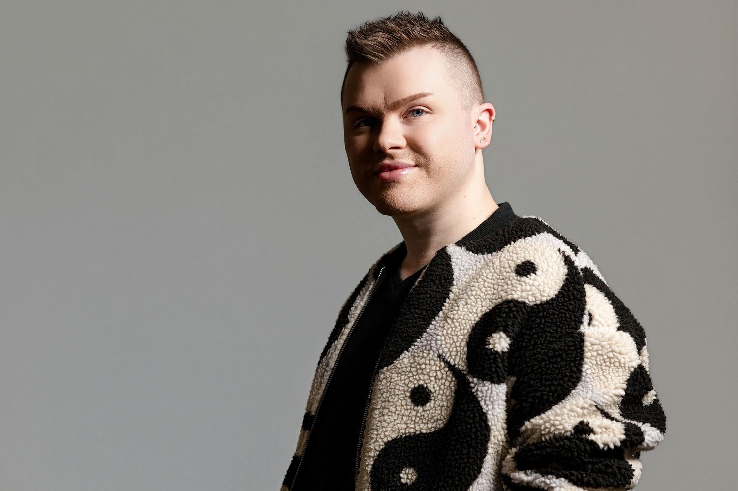 Person wearing a black and white patterned sweater against a gray studio backdrop.