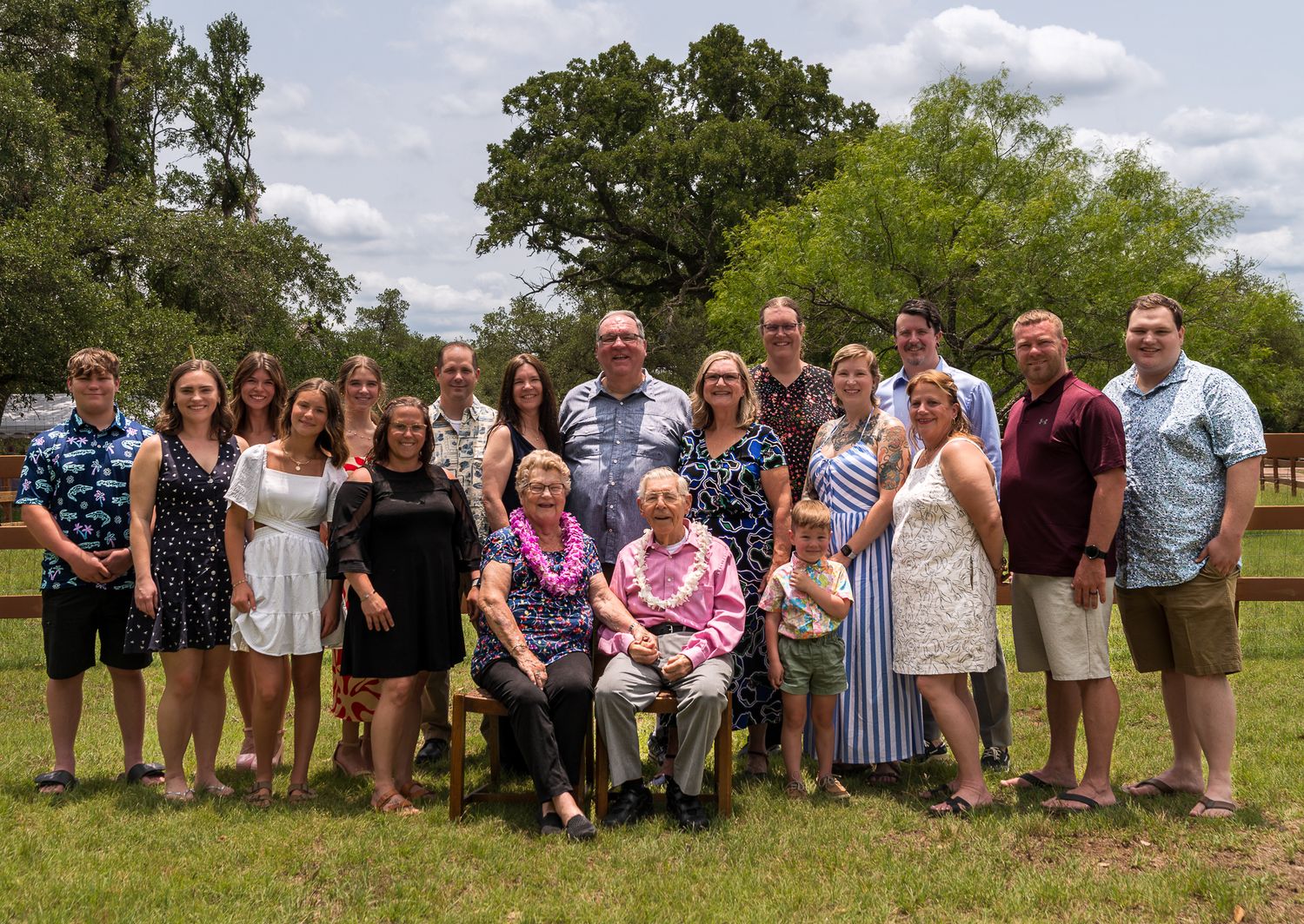 Large family group posing together outdoors on a sunny day with trees and grass in the background.