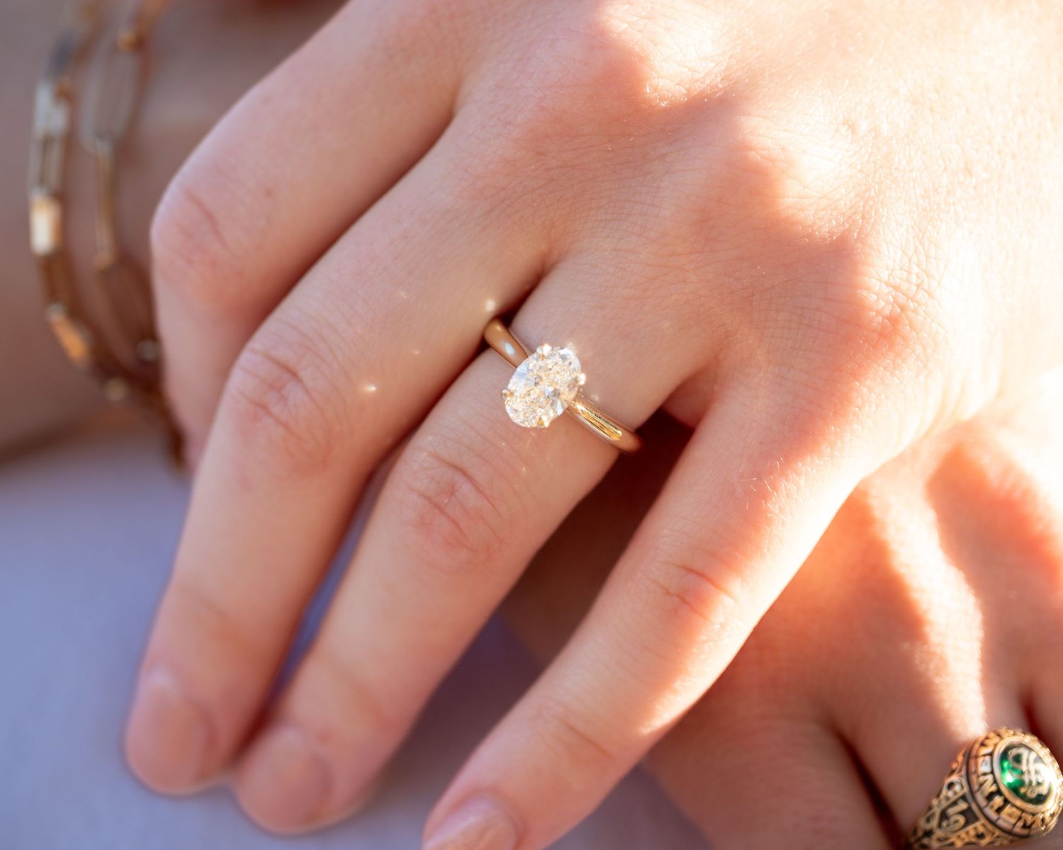 A close-up shot of hands wearing delicate gold rings in warm sunlight.