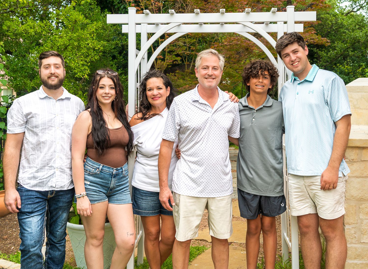 Casual group portrait of people lined up against a white fence in a garden setting.