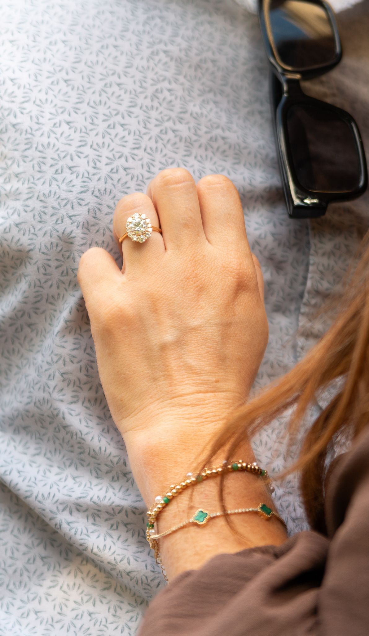 Close-up of delicate gold bracelet and ring on hand against patterned fabric background.