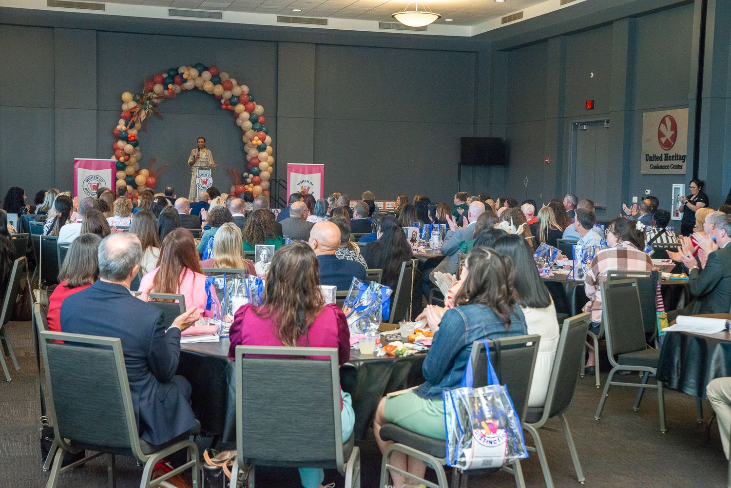 Banquet hall filled with guests at round tables under floral arch decor.