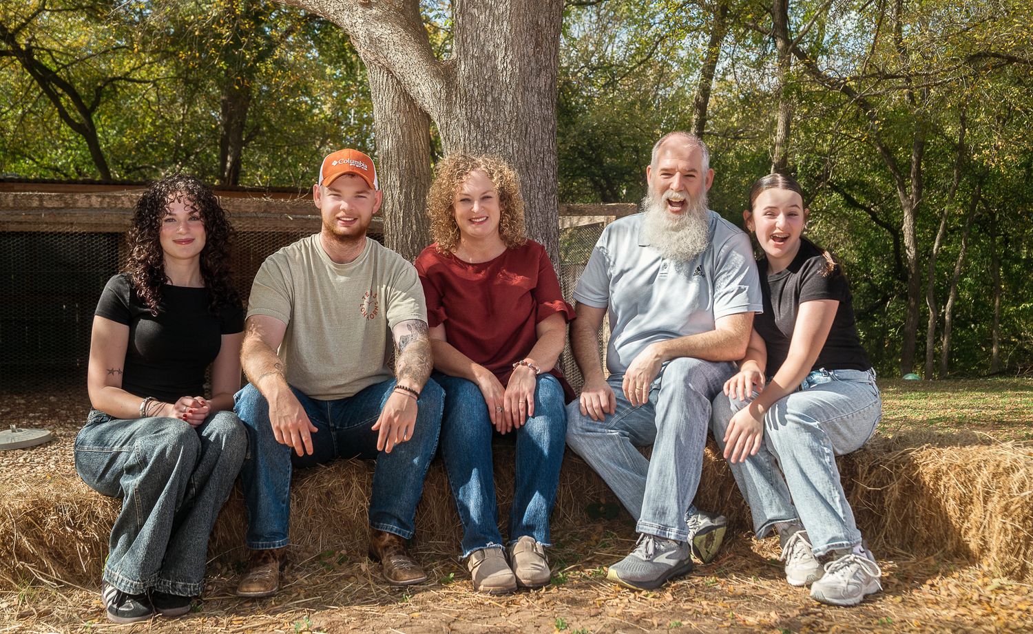 Family members sitting casually on hay bales in a rustic outdoor setting.