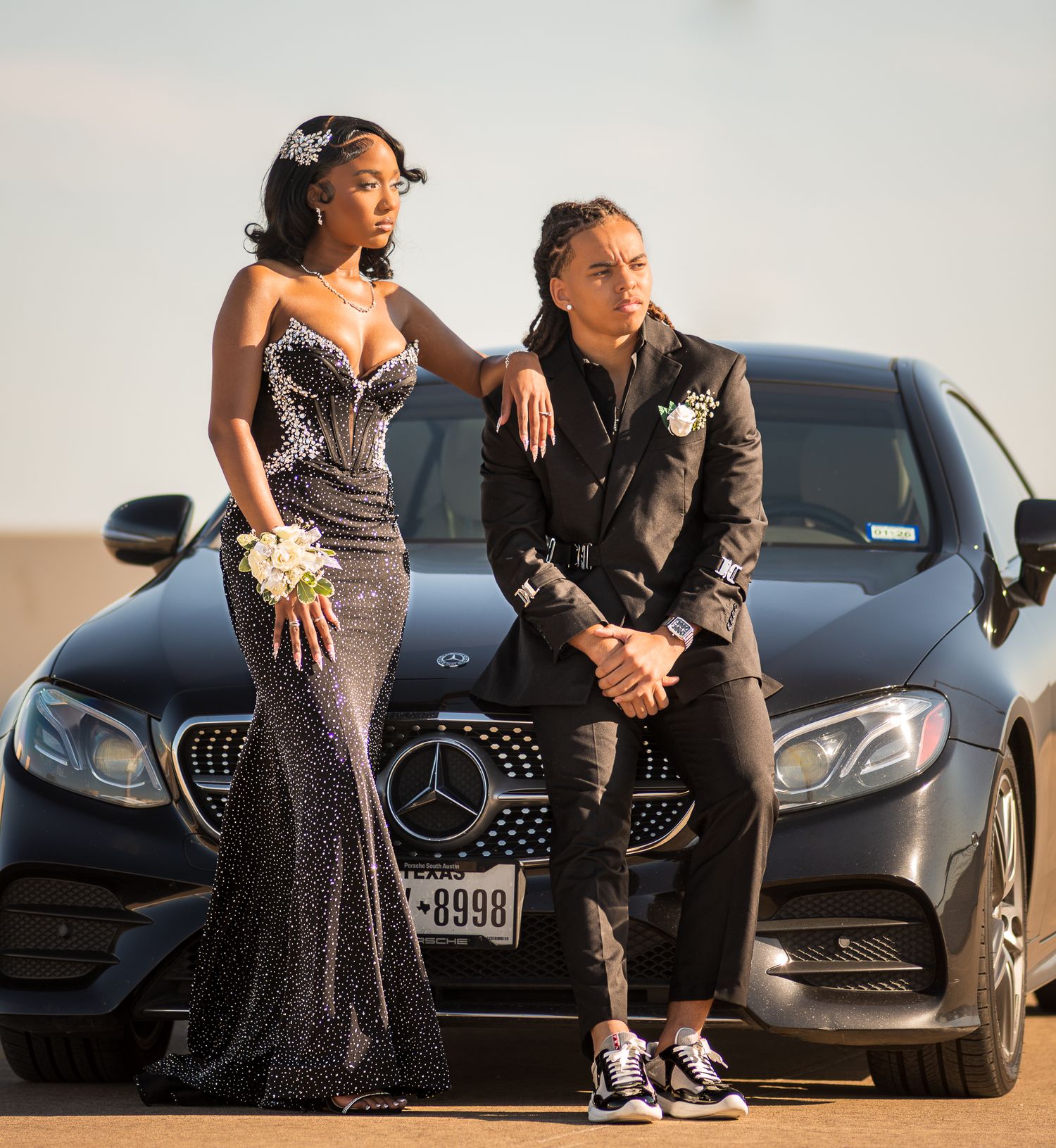 Stylish couple posing against luxury black Mercedes cars during a photoshoot.