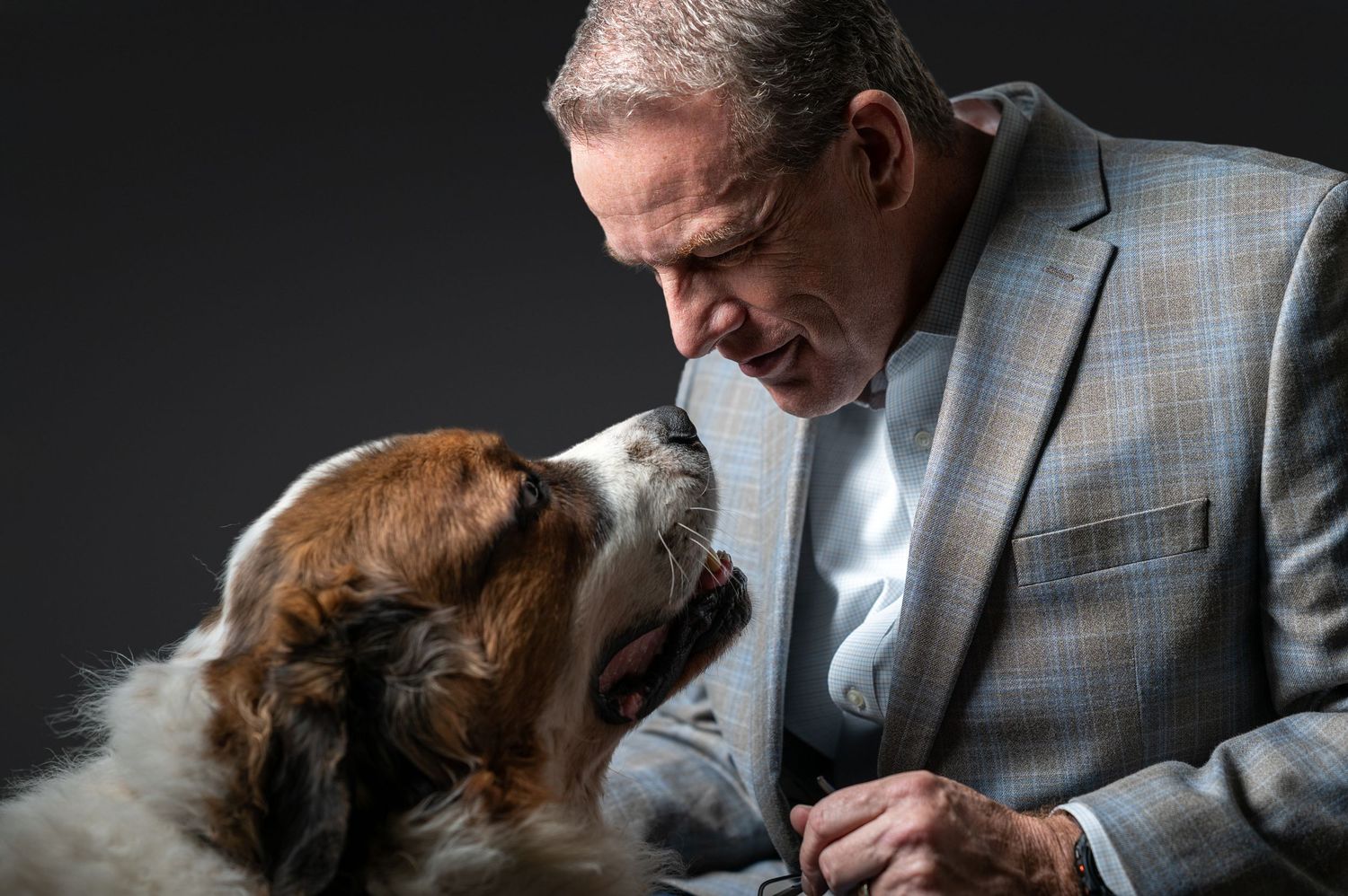 A person in a gray suit holds and kisses a small brown dog in a series of tender moments captured in black and white.