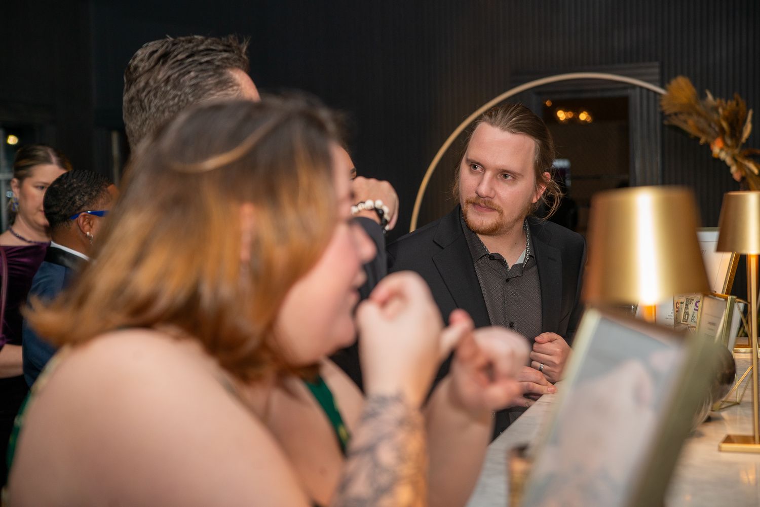 Dimly lit social gathering with people mingling at tables.