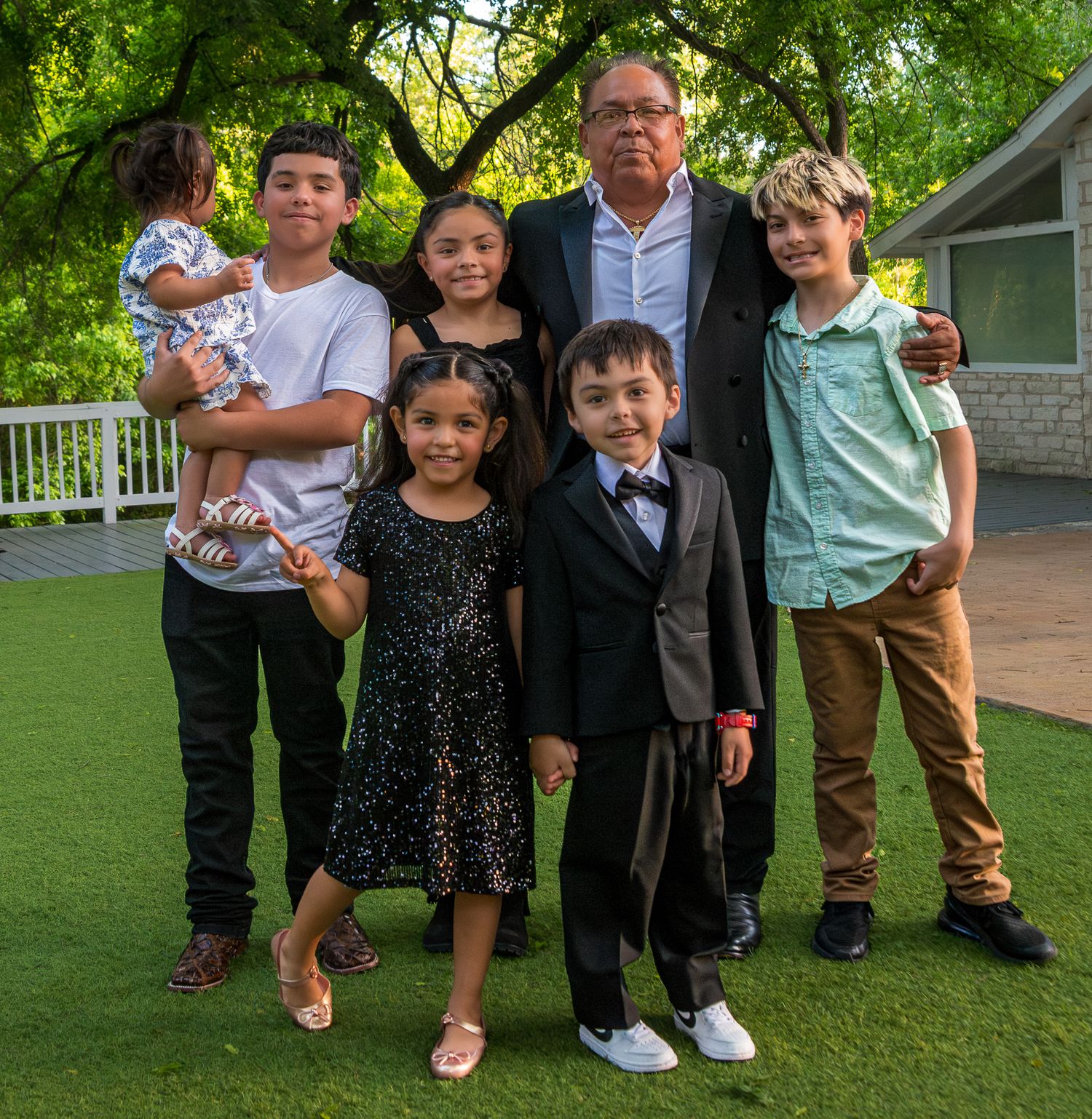 A multi-generational family group poses together outdoors on artificial turf.