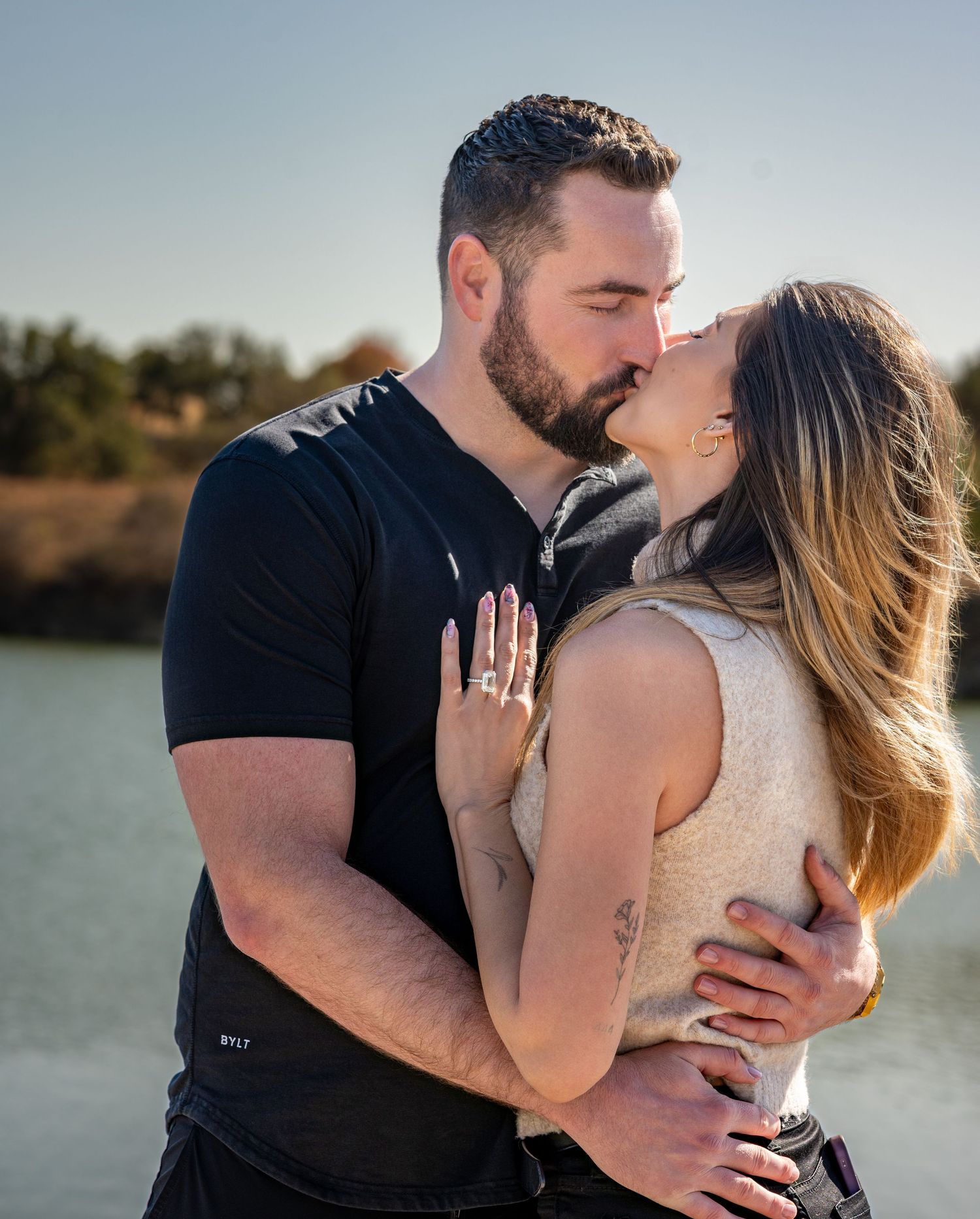 Romantic lakeside photoshoot with couple embracing at sunset.