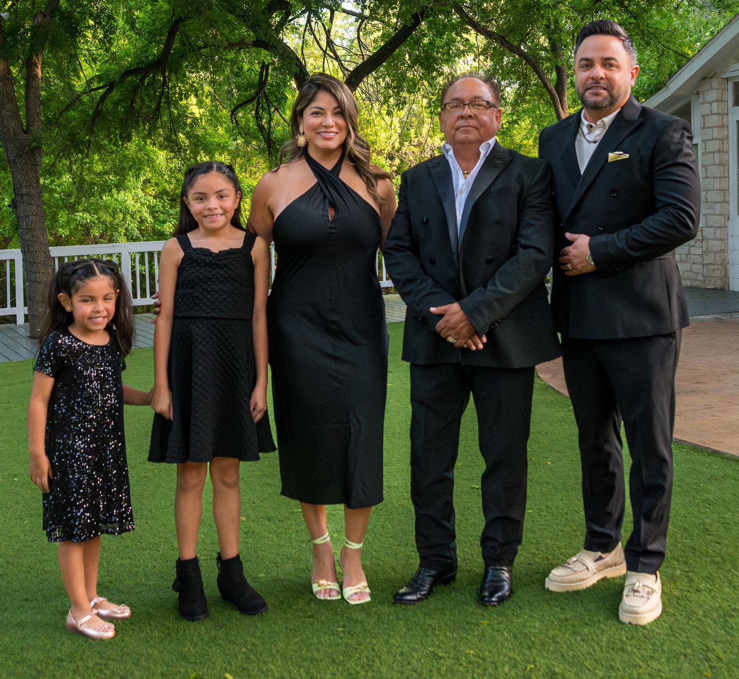 A family group in formal black attire poses together on a manicured lawn.