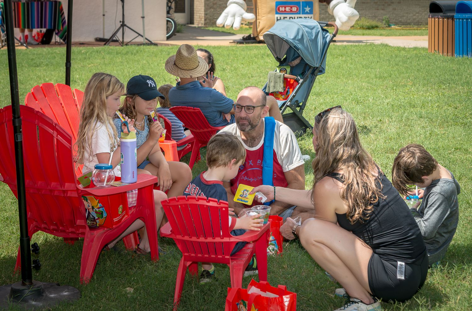 Attendees relaxing in red chairs at an outdoor summer event.