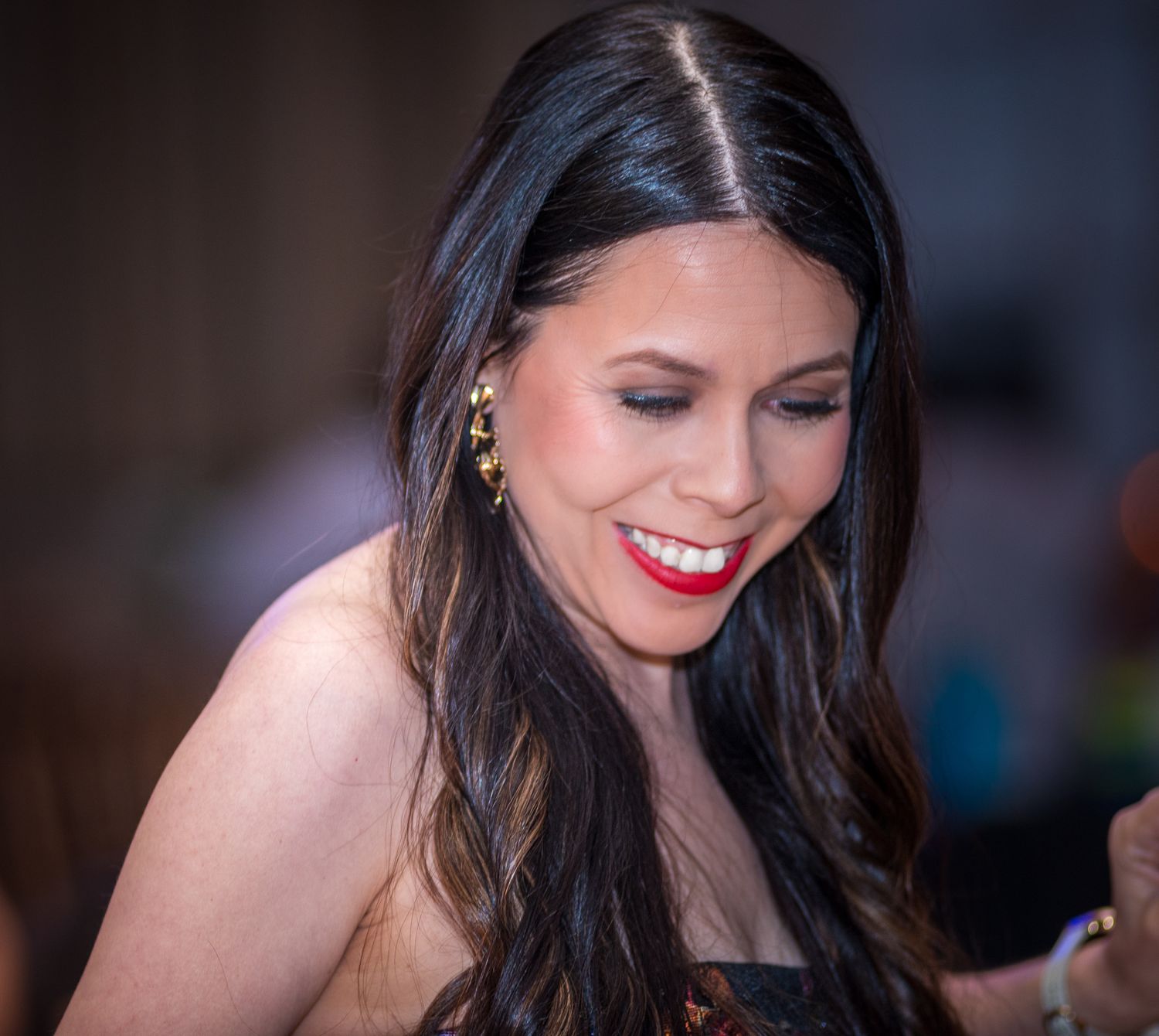 Woman with dark hair and red lipstick laughing during an evening celebration.