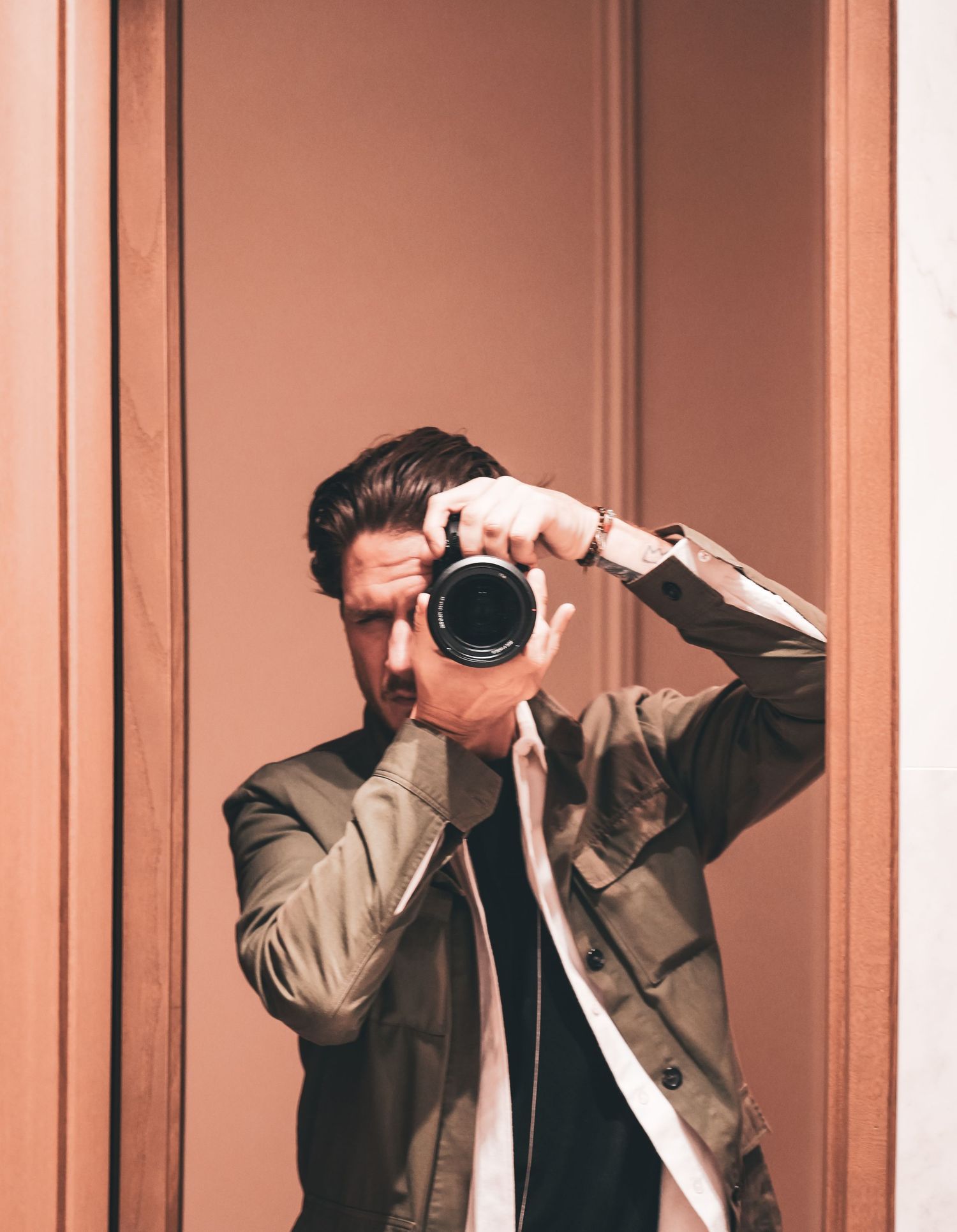 Man taking a mirror selfie with a DSLR camera wearing a olive green jacket.