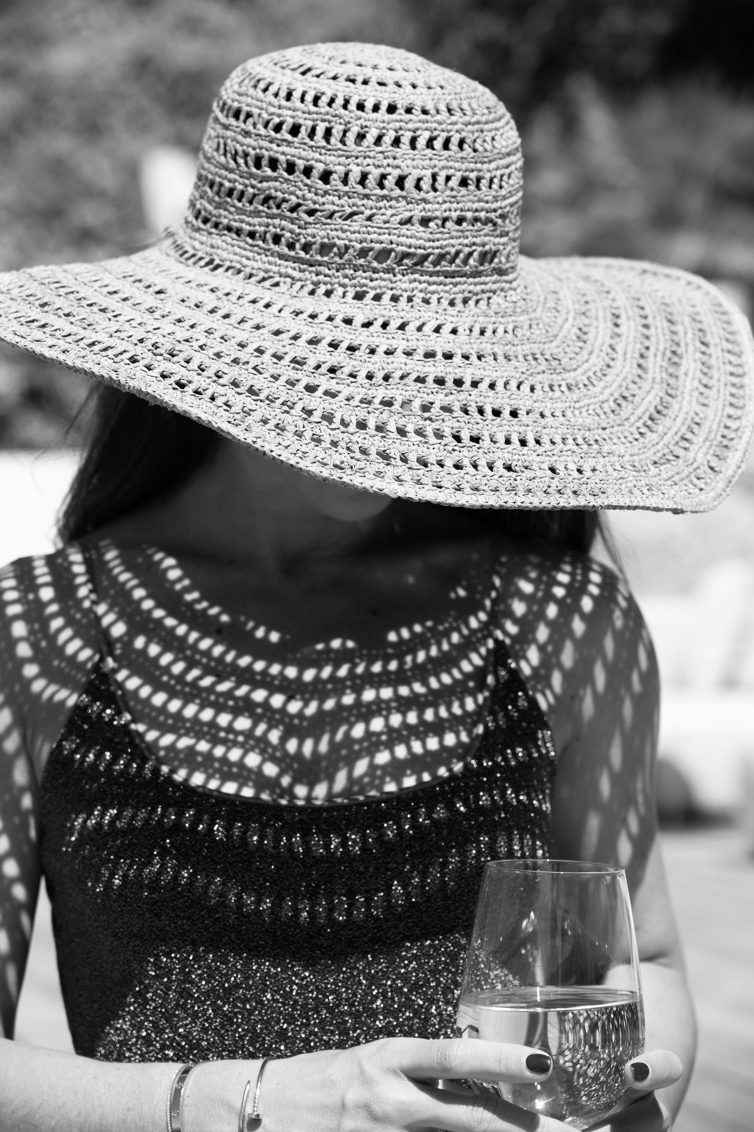 Black and white photo of a woman in a wide-brim straw hat and lace top holding a glass of white wine.