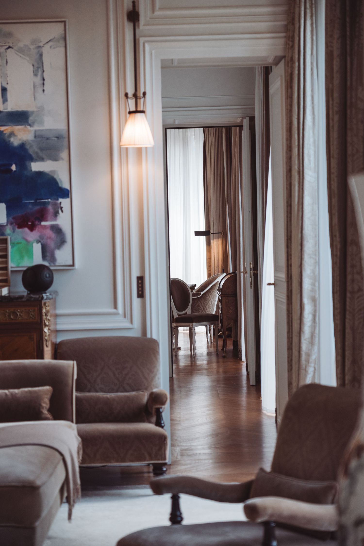 Elegant French-style living room with velvet armchairs, parquet floors, abstract art, and a glowing floor lamp.