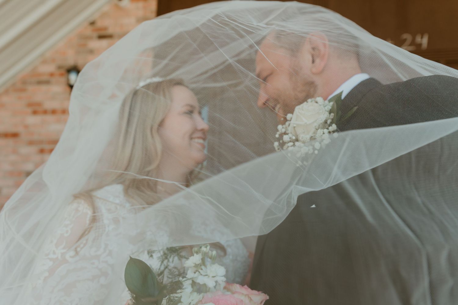 Bride and groom smiling under flowing veil on wedding day.