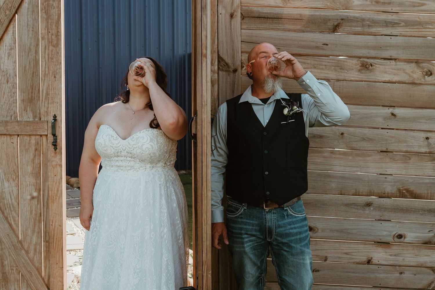 Bride and groom taking a shot of whiskey together outside a rustic wooden barn.