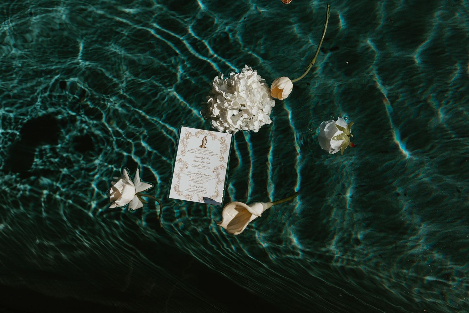 Wedding invitation suite with gold ornate details floating in crystal clear turquoise water.