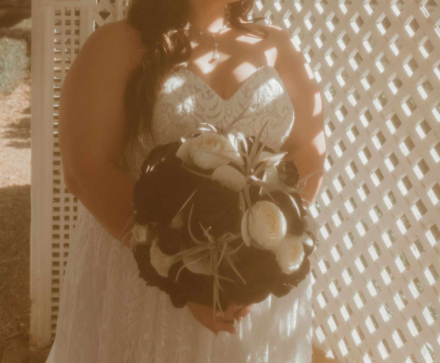 Close-up of bride holding a dramatic dark floral bouquet in soft dappled light against white lattice.