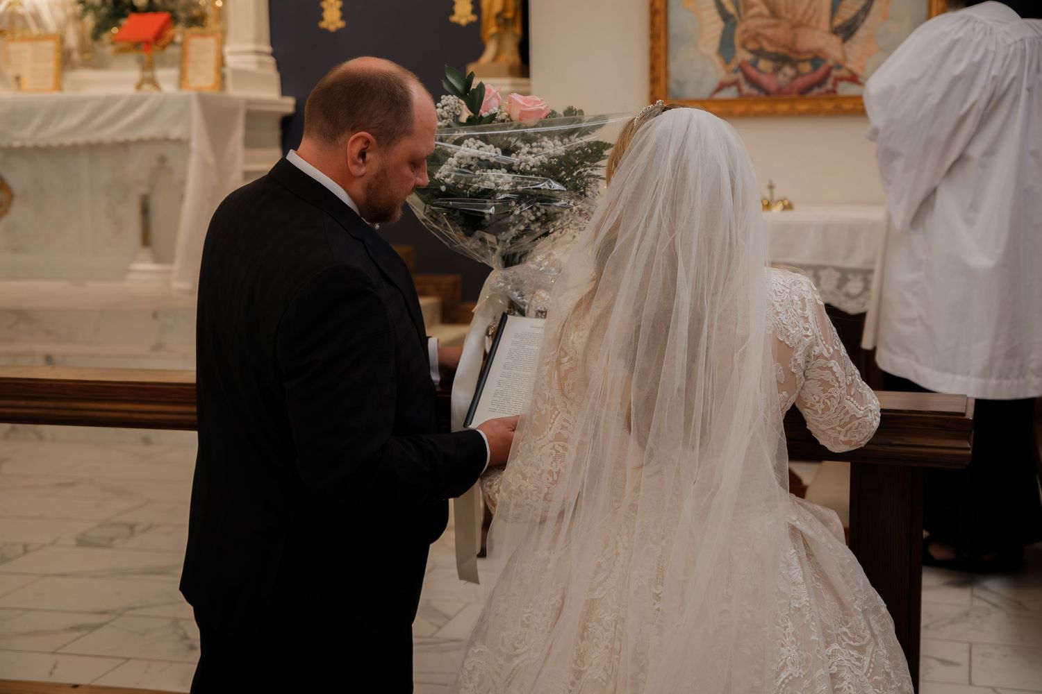 Father walking bride in lace wedding gown and veil down the aisle of a decorated church.