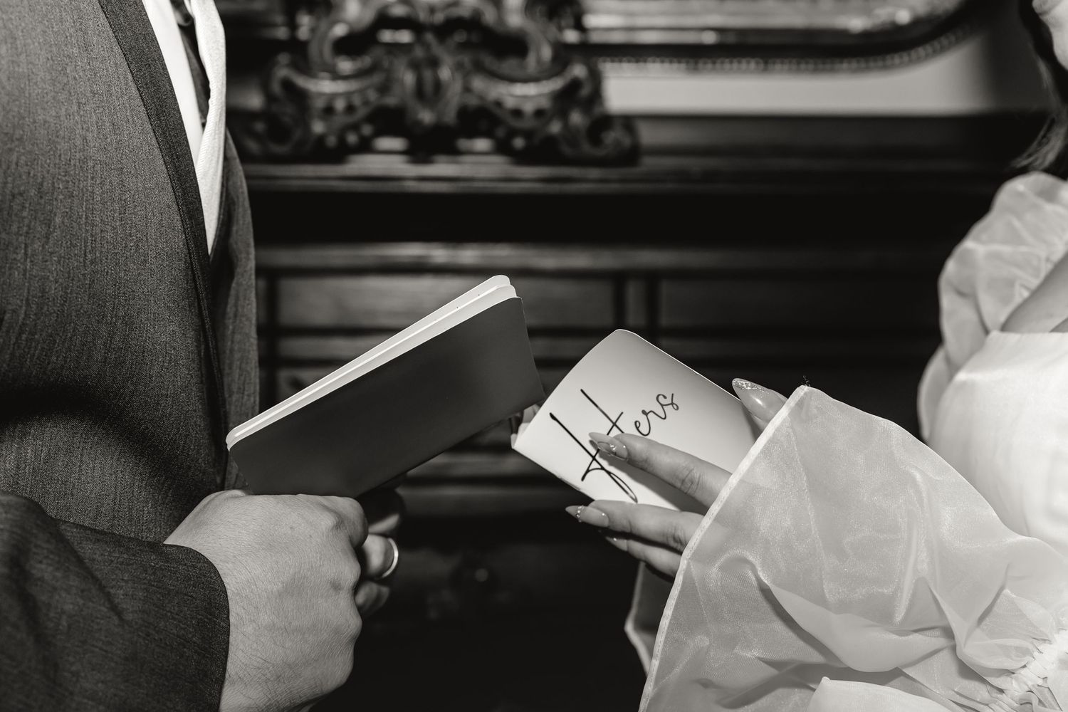 Black and white close-up of a bride and groom exchanging handwritten vows during an elegant indoor wedding ceremony.
