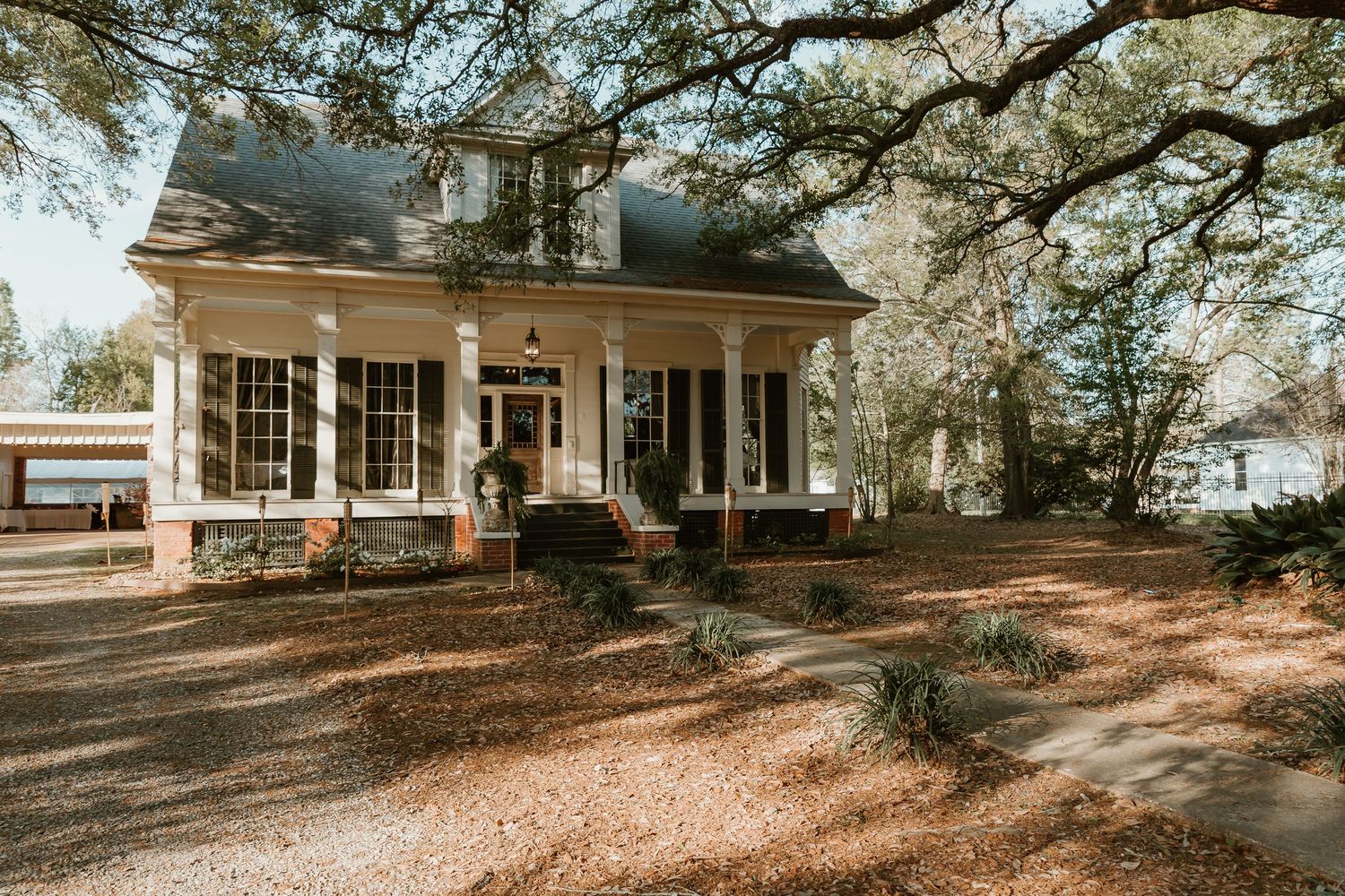 A charming brick colonial wedding venue with white columns surrounded by large oak trees.