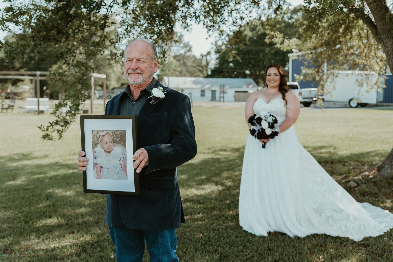 Father holds a framed childhood photo of the bride during an emotional first look at outdoor wedding.