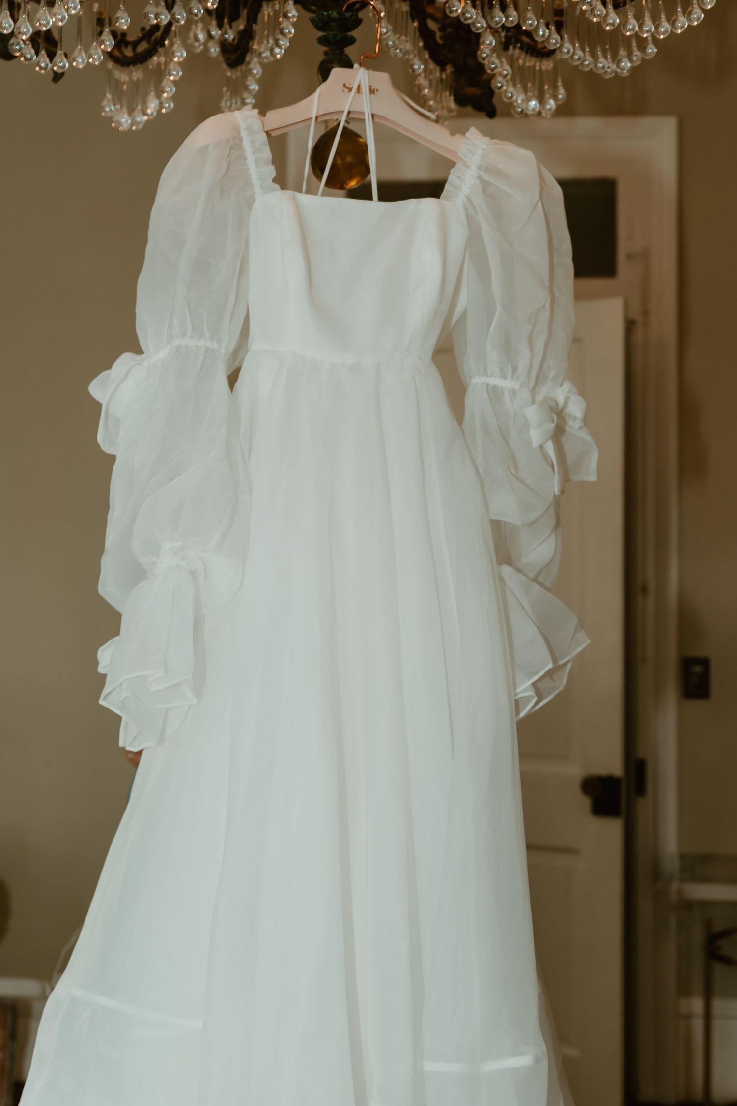 Stunning white wedding gown with dramatic puff sleeves and ruffled cuffs hanging from a crystal chandelier.