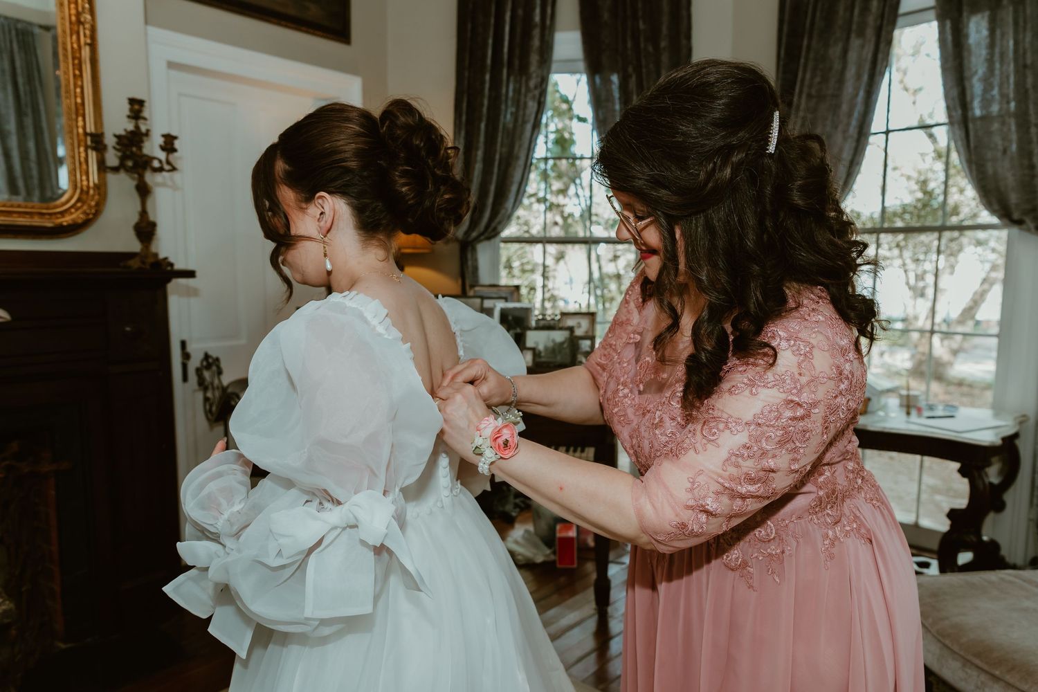 Mom helps a bride with her white wedding gown in an elegant room.