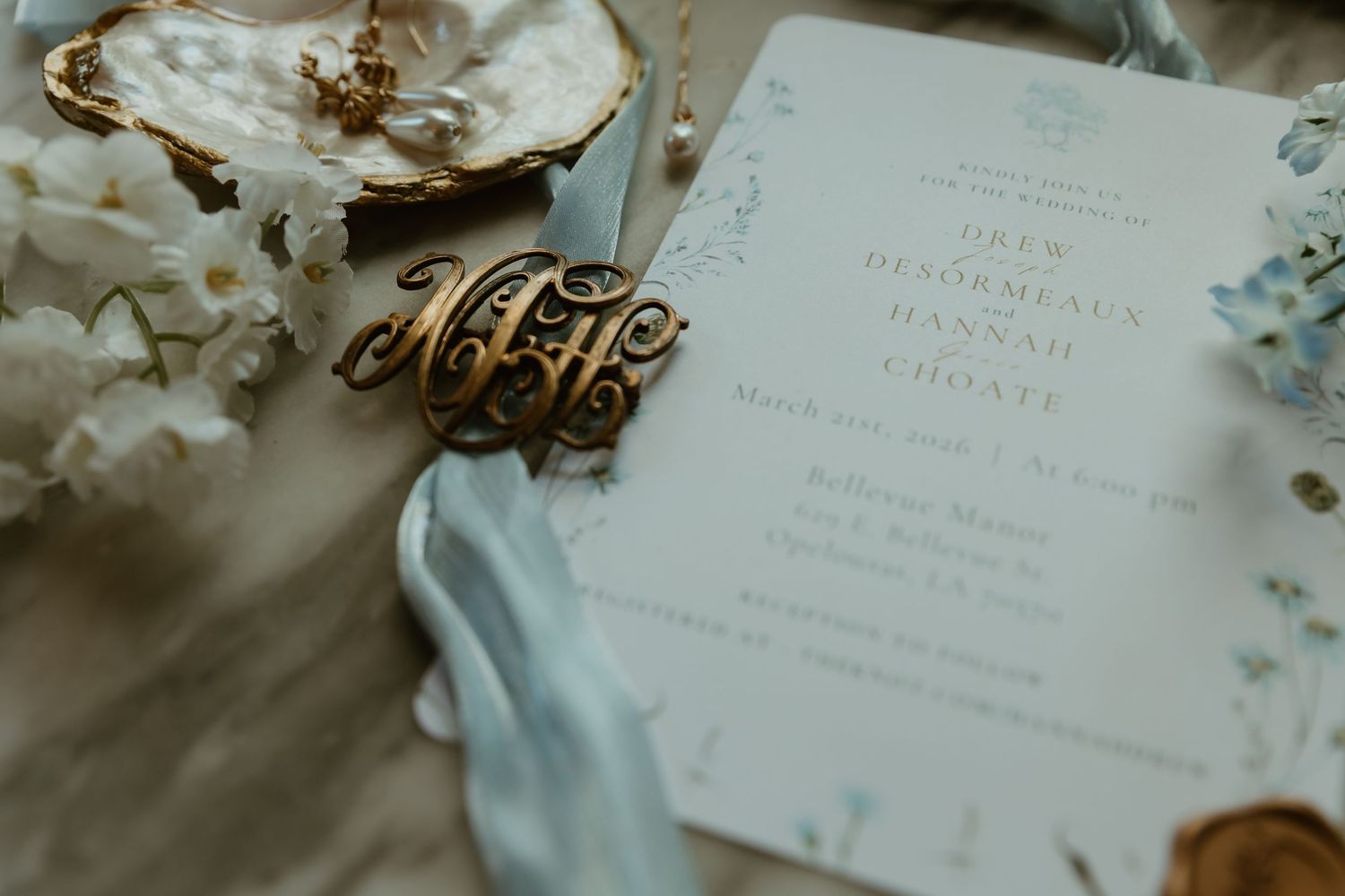 Close-up of elegant wedding invitation with gold monogram charm and soft blue ribbon.