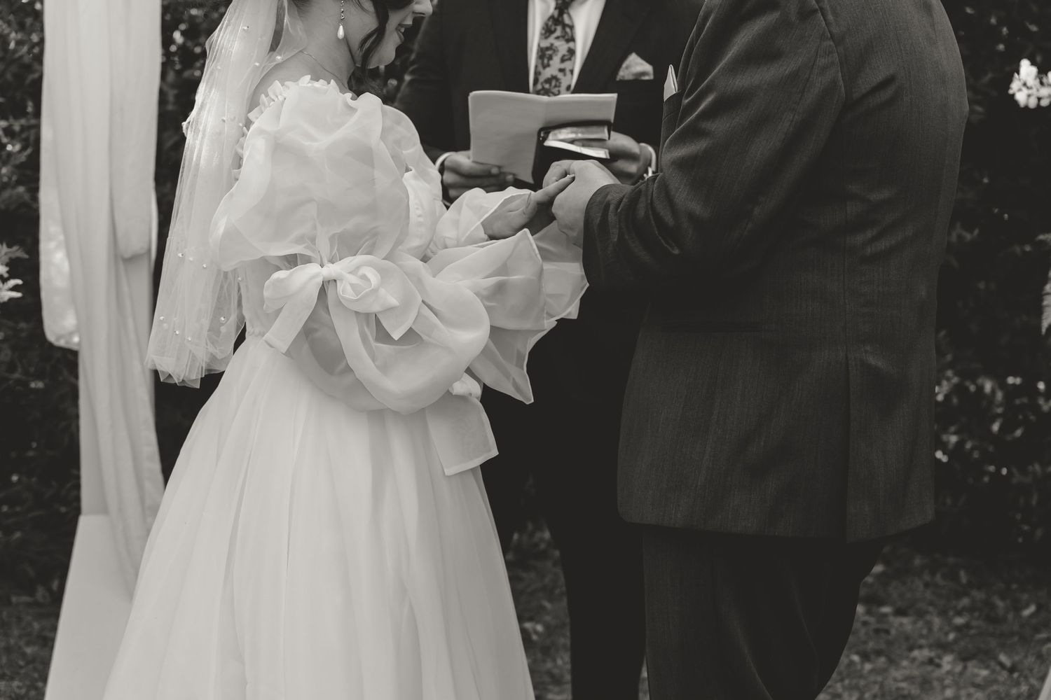 Black and white photo of bride and groom exchanging rings at outdoor wedding ceremony.