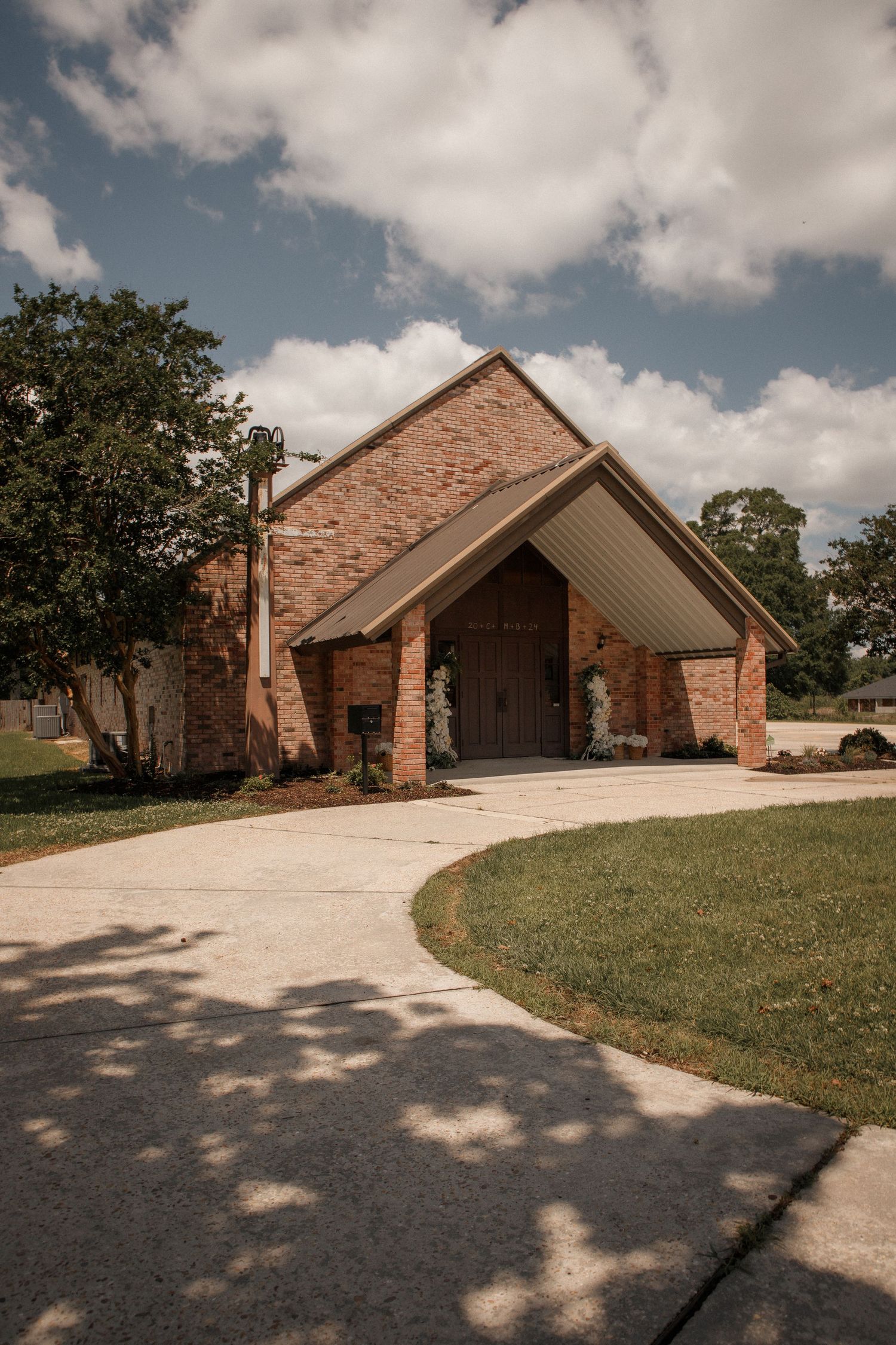 Exterior of brick chapel wedding venue with arched wooden doors and curved driveway under blue sky.