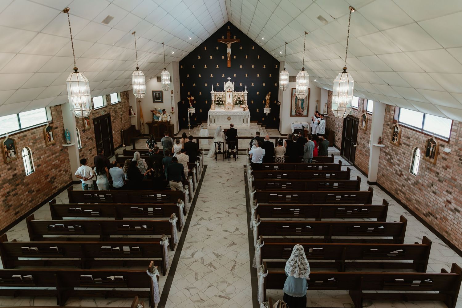 Overhead view of intimate church wedding ceremony with wooden pews and guests gathered at white altar.