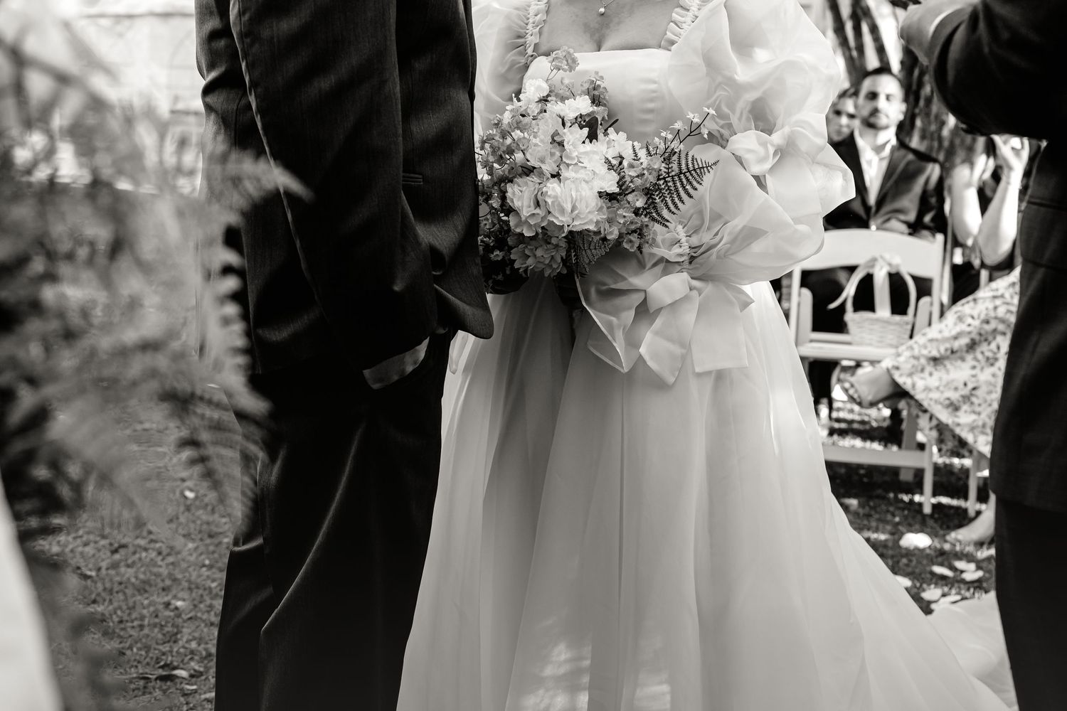 Black and white photo of bride and groom standing together during outdoor wedding ceremony.