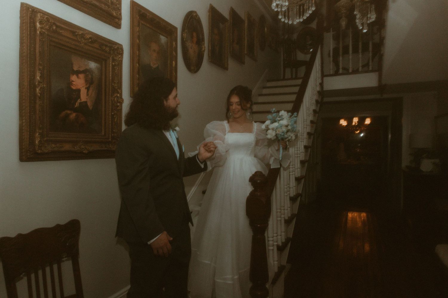 Bride and groom share a tender moment on a staircase surrounded by framed portrait paintings.