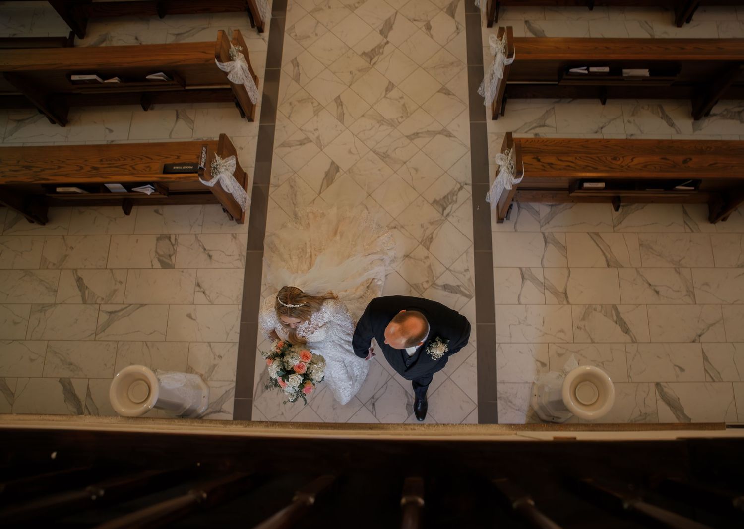 Aerial view of bride and groom walking down church aisle on wedding day.