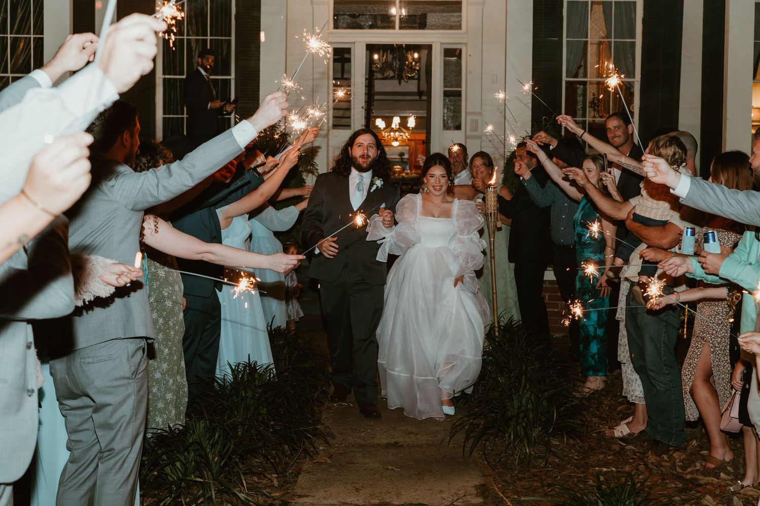 Bride and groom exit through a sparkling sparkler send-off tunnel with cheering wedding guests.
