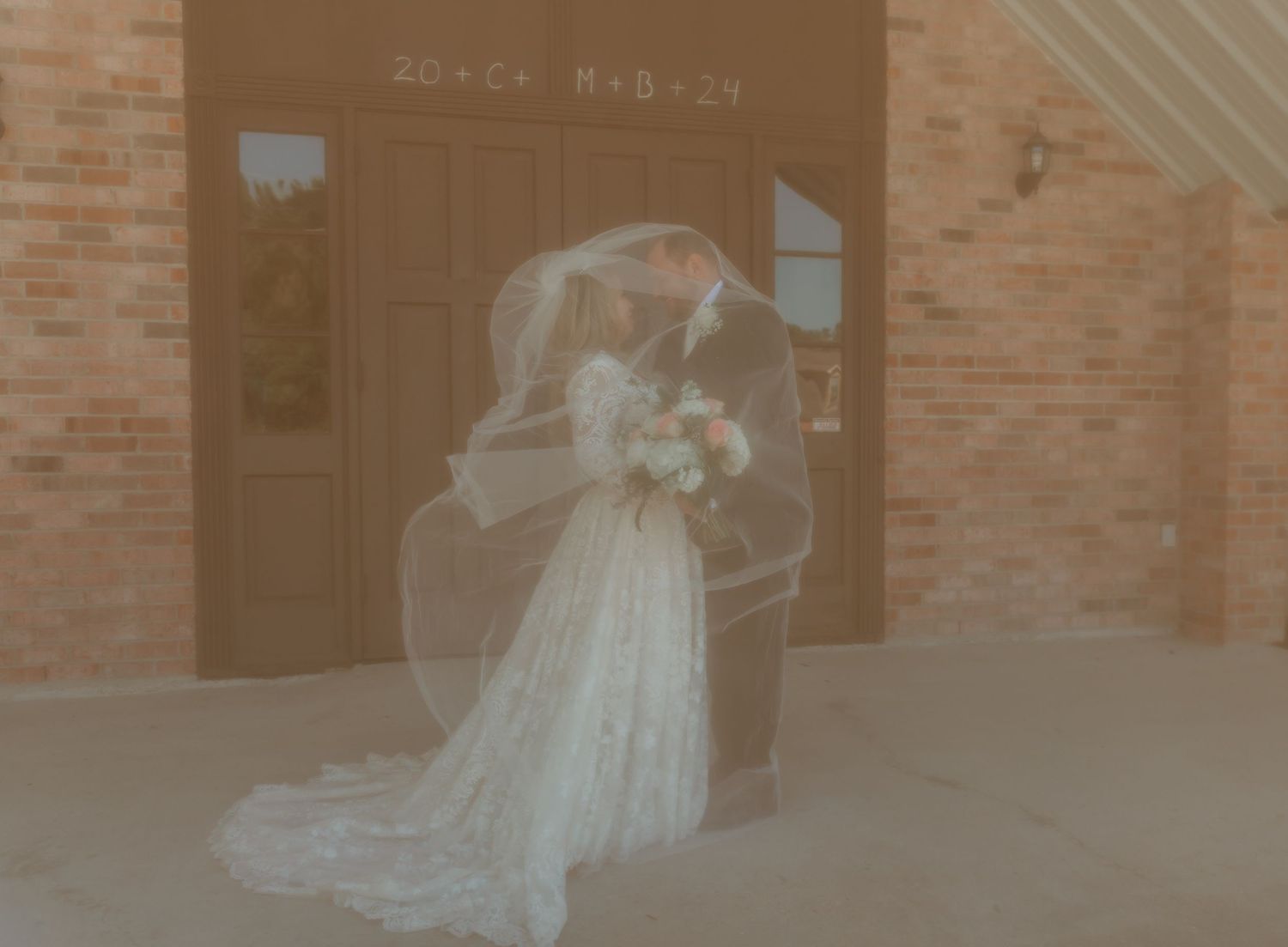Bride and groom kissing under veil outside brick church entrance.
