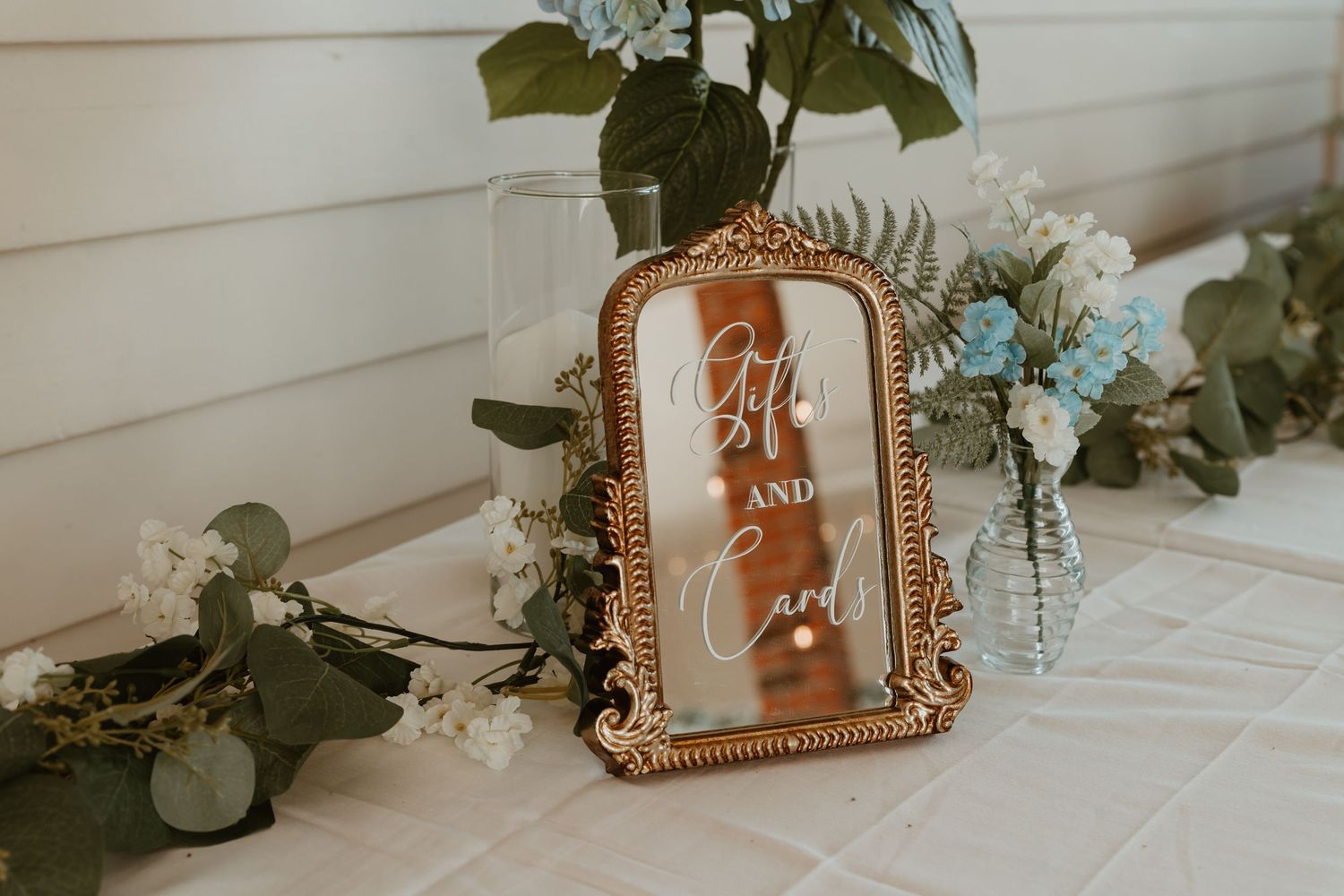 Gold ornate mirror sign reading Gifts and Cards displayed on a table with blue and white florals.