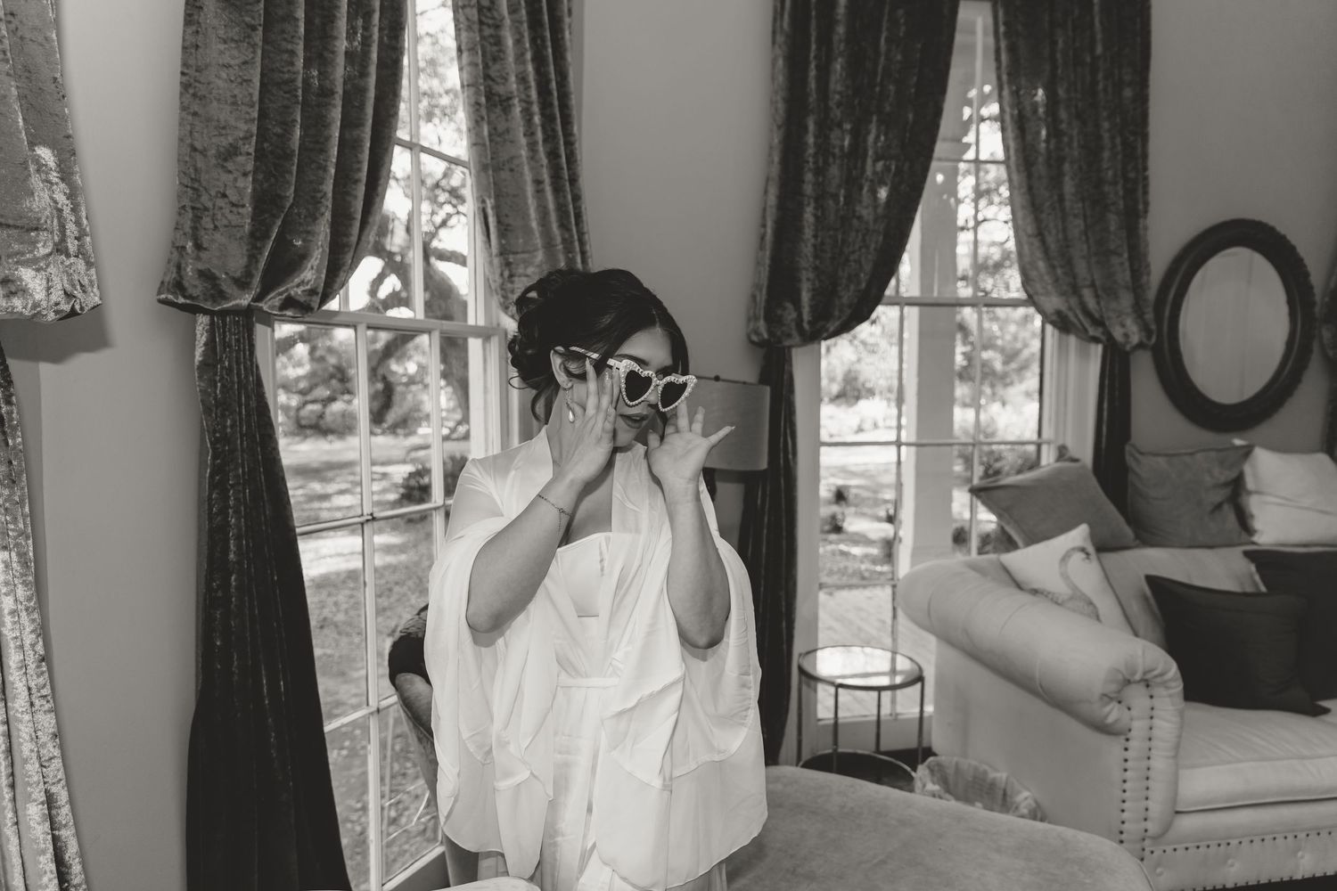 Black and white photo of bride in robe wearing sunglasses while getting ready for wedding.