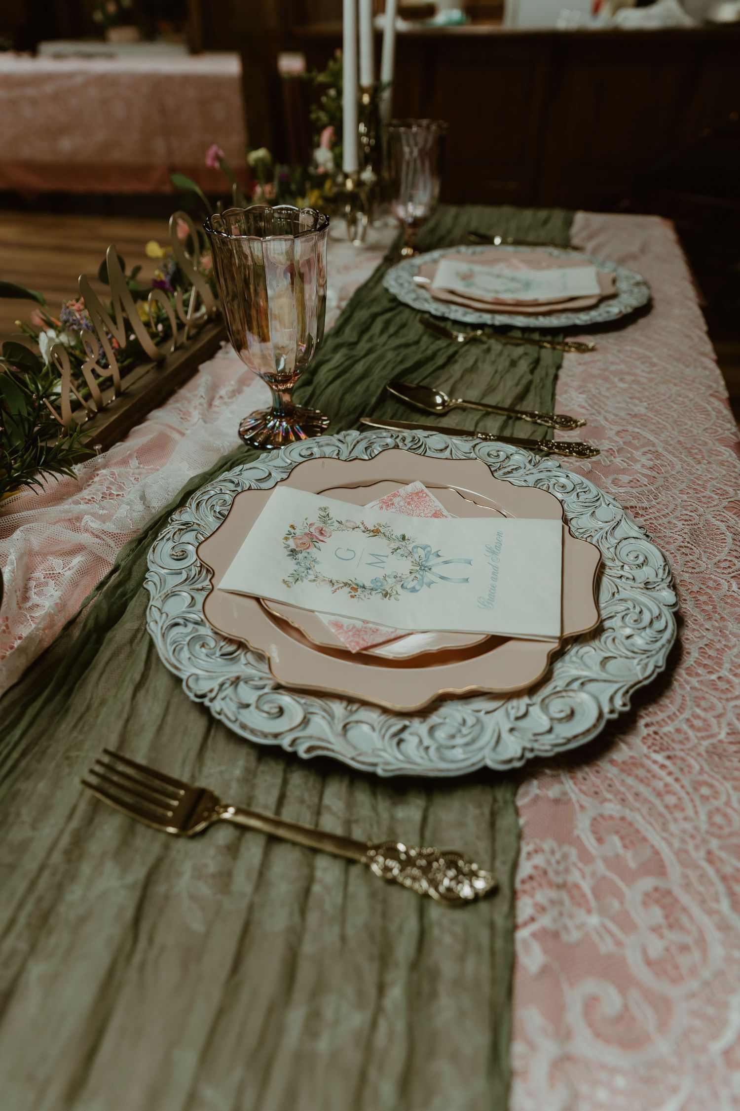 Elegant wedding table setting with ornate charger plates, pink napkins, and gold silverware.