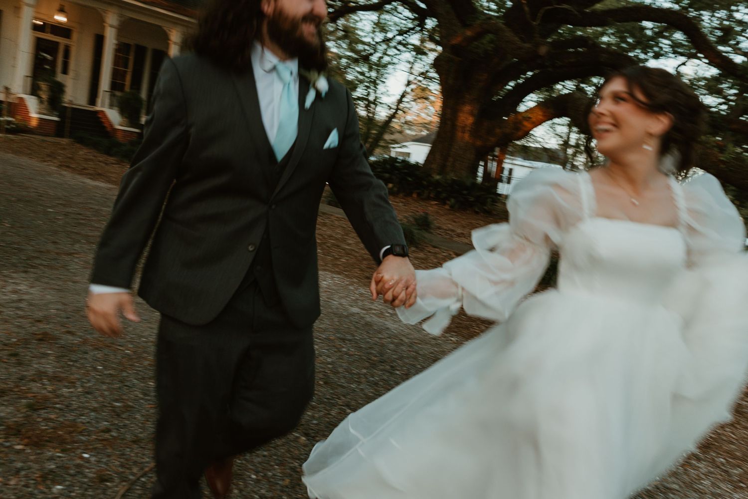Joyful bride and groom run hand in hand outside a historic venue in wedding attire.
