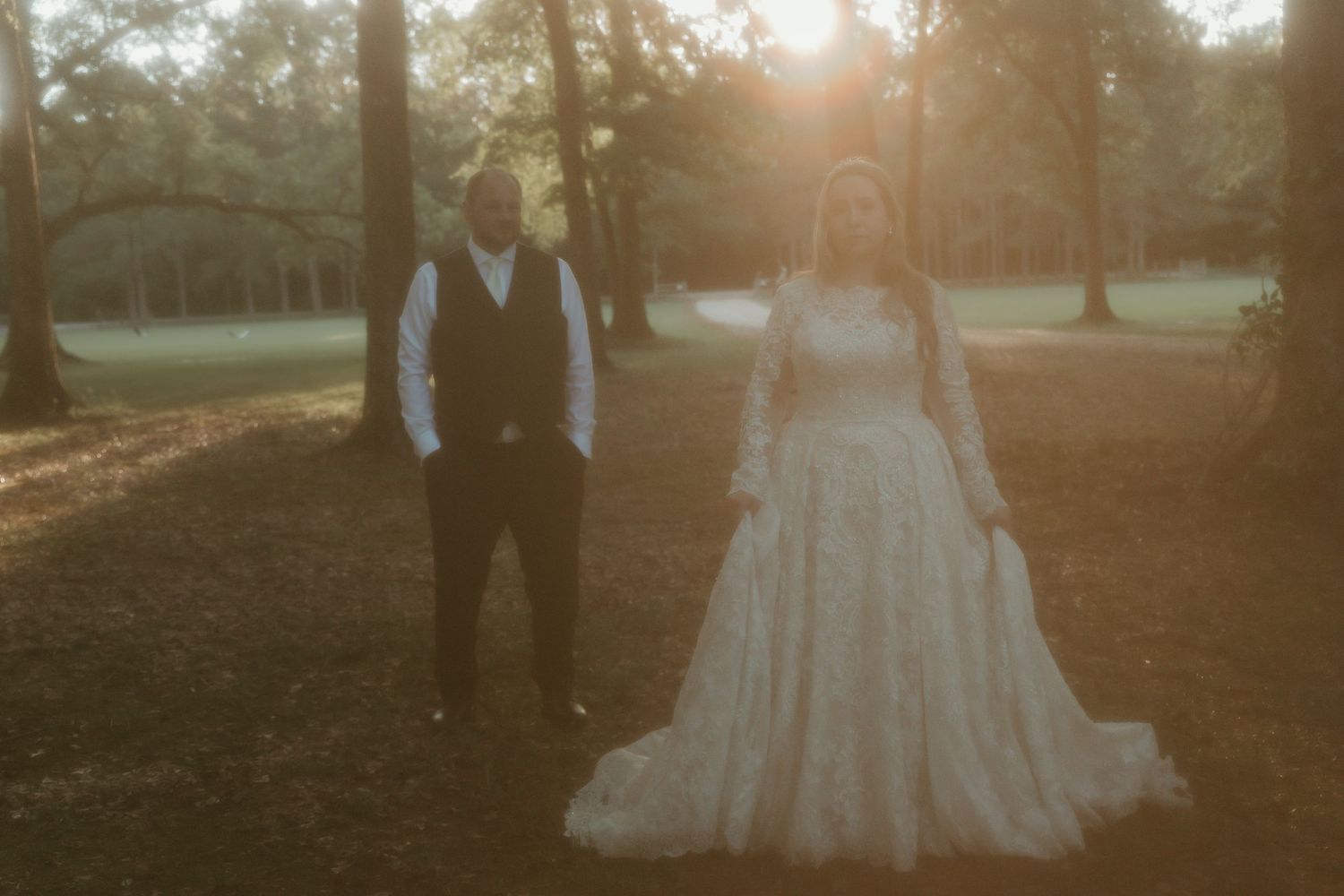 Bride and groom standing in golden sunset light among tall trees.