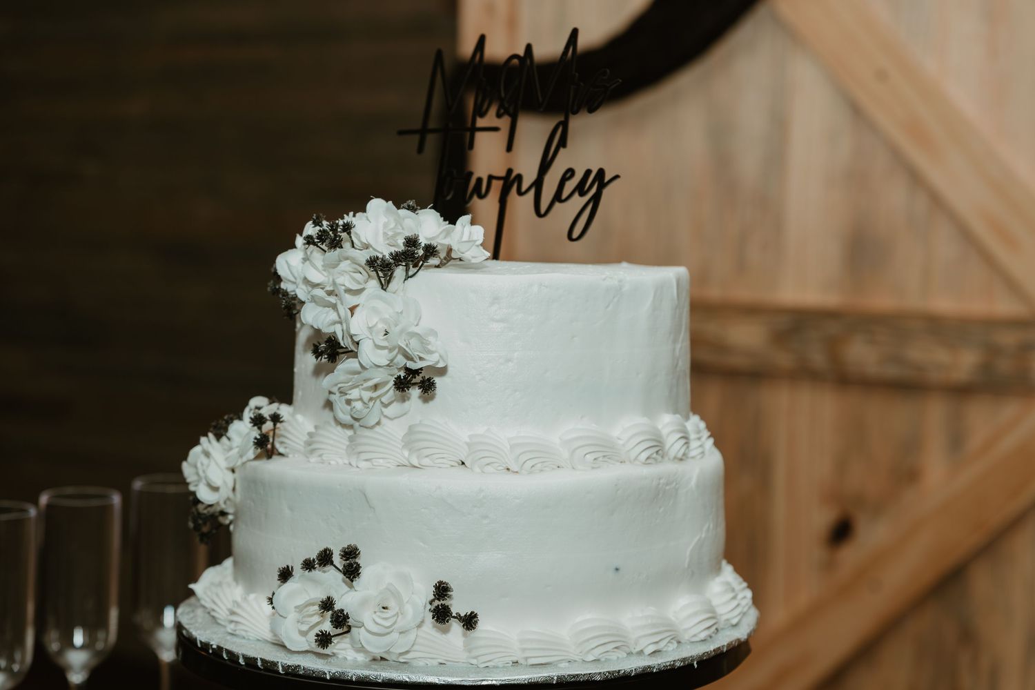 Elegant two-tier white wedding cake with floral decorations and a custom name cake topper.