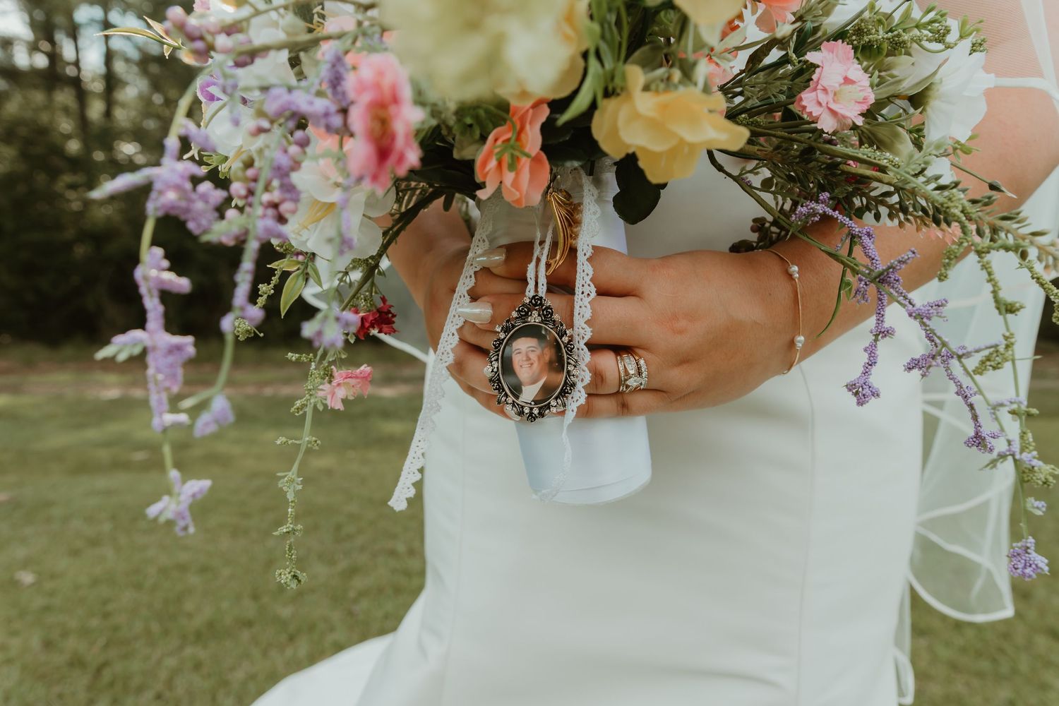 Close-up of bride holding colorful bouquet with memorial photo charm attached to ribbon wrap.