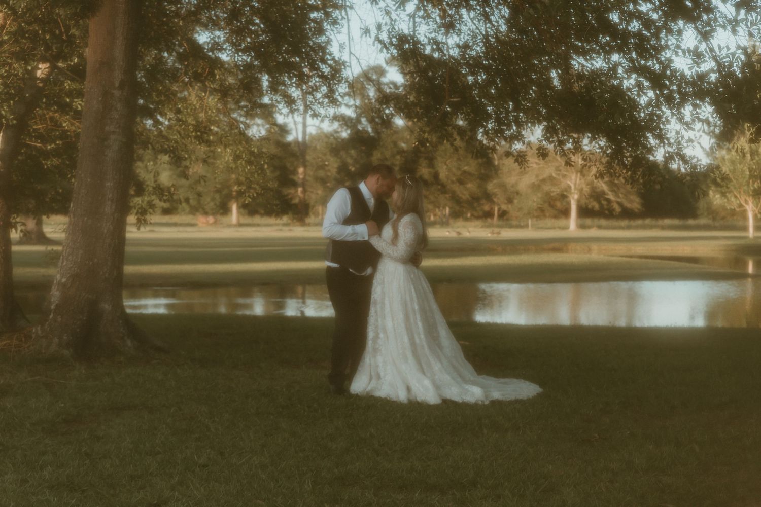 Romantic bride and groom sharing an intimate moment by a serene pond under golden hour light.